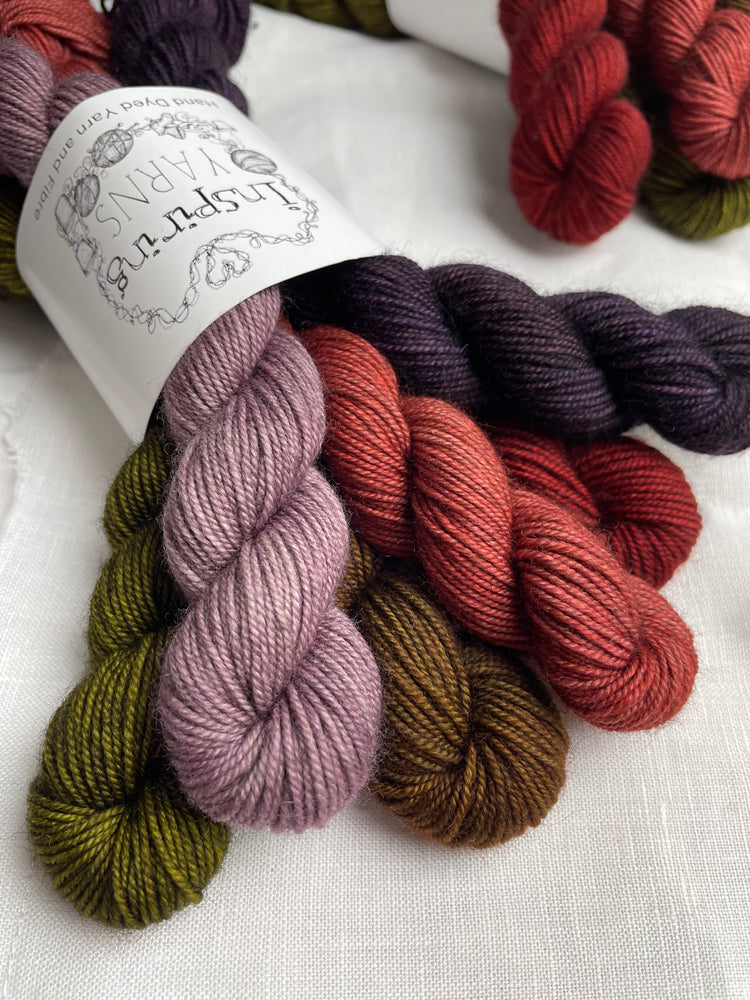 Close up of a set of 6 mini skeins of various colours of Yak Sock yarn on a white linen background.