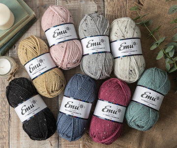 A variety of colours of tweed nep yarns by Emu on a wood plank background.