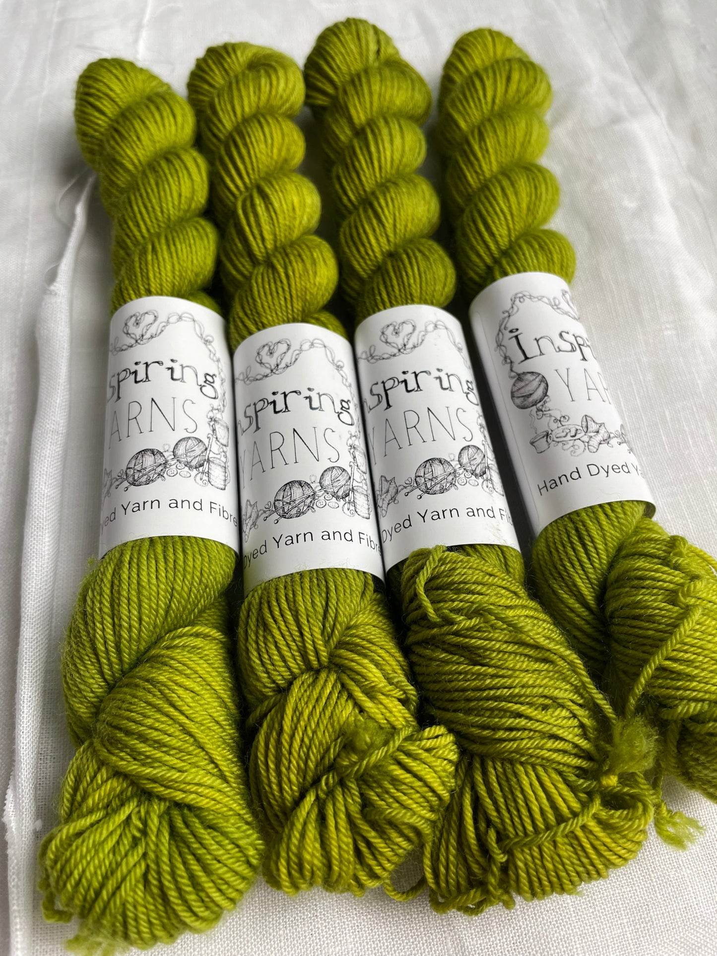 close up of four skeins of yarn with inspiring yarns labels on plain fabric background.