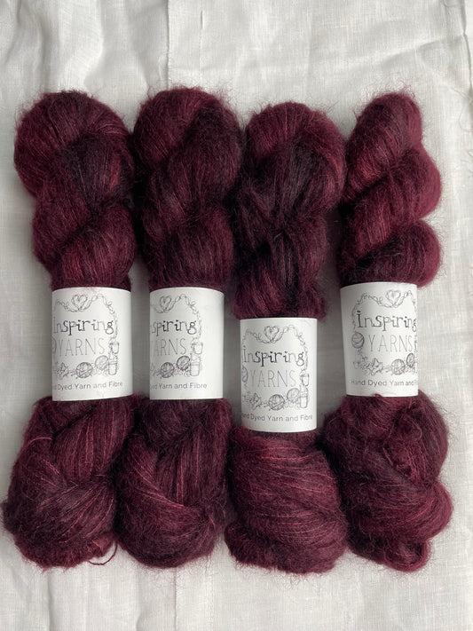 Four skeins of fluffy brushed suri silk lace yarn in a tonal dark burgundy colour labelled Inspiring Yarns on a white linen background.