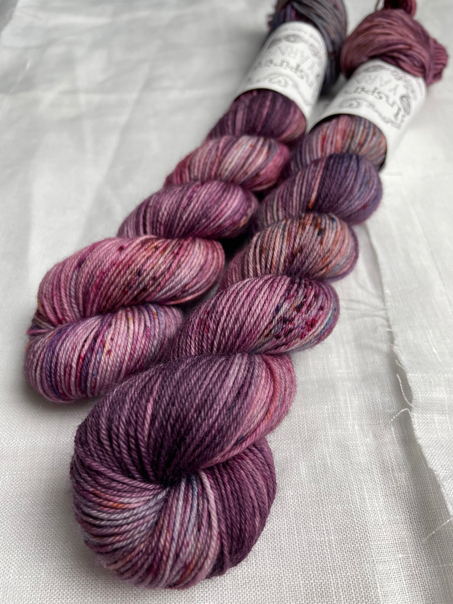 Two skeins of merino smooth sock in shades of pink and blue labelled Inspiring Yarns on a white linen background.