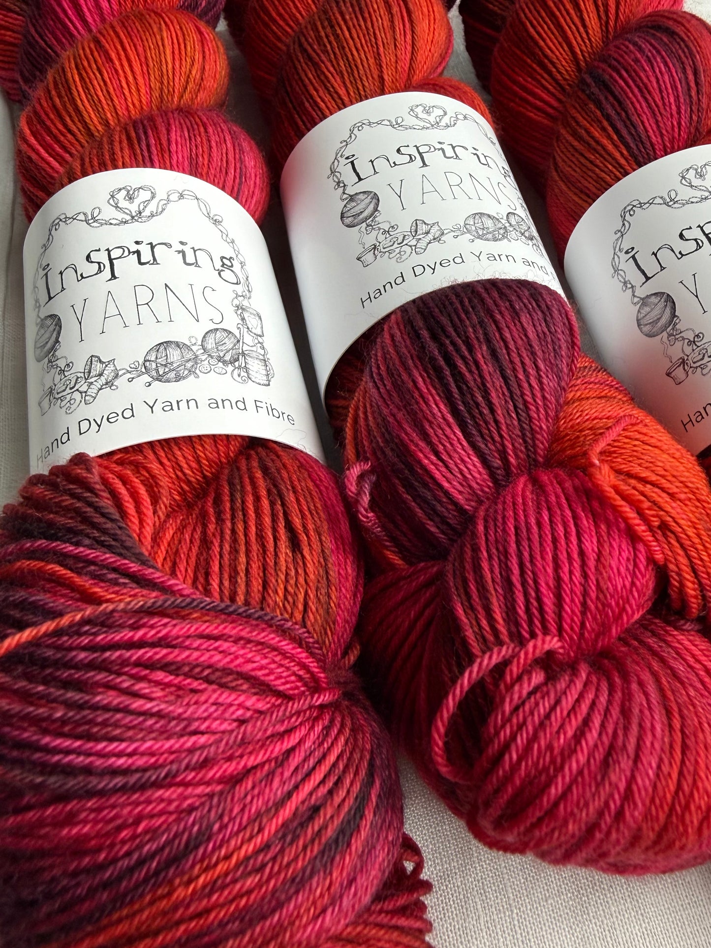 Three skeins of red variegated yarn labelled Inspiring Yarns on a white background