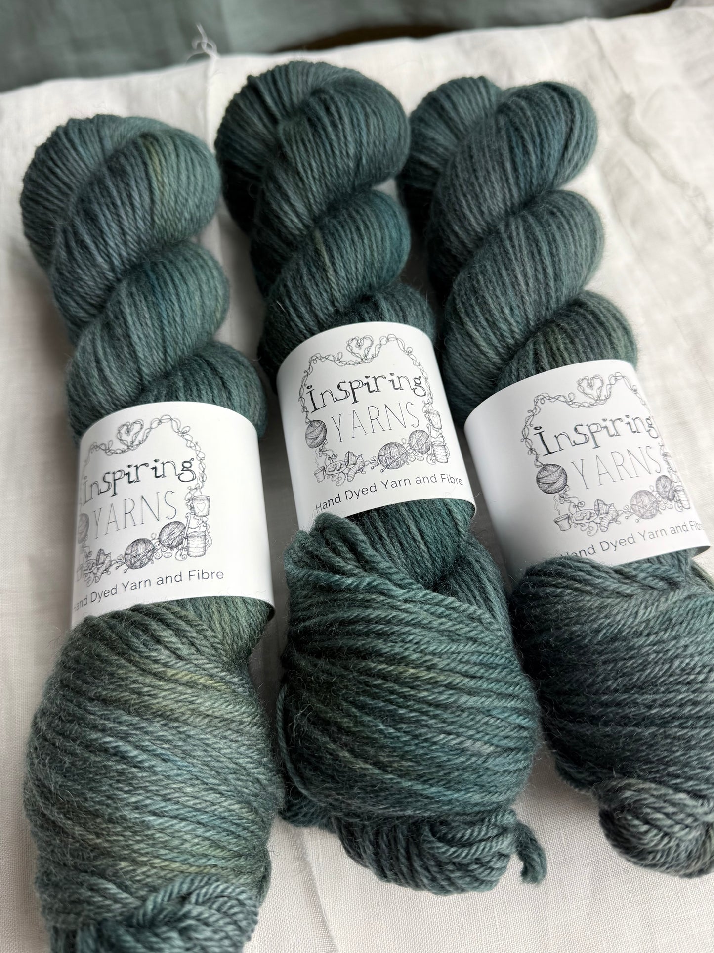 Three skeins of dark green tonal yarn labelled Inspiring Yarns on a white background