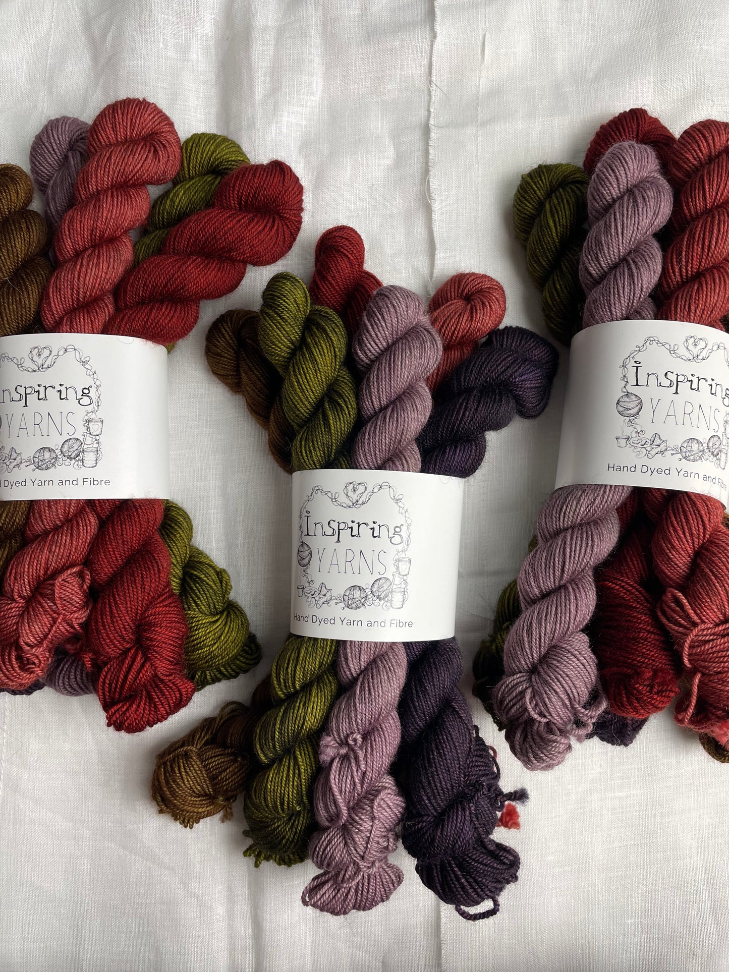 Three sets of 6 mini skeins of various colours of Yak Sock yarn labelled Inspiring Yarns on a white linen background.