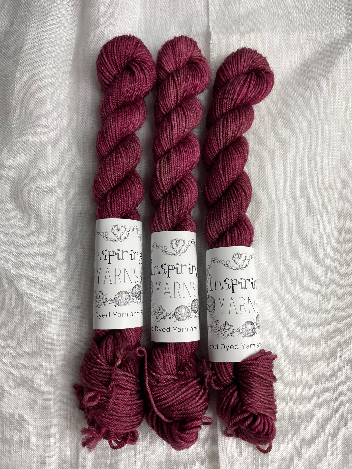 Three mini skeins of dusky pink Merino Smooth Sock yarn labelled Inspiring Yarns on a white linen background.