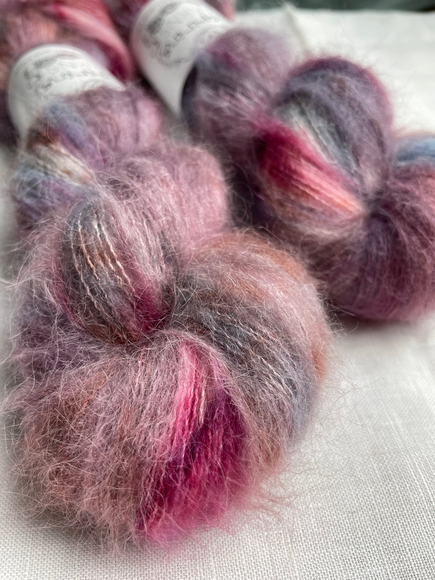 Two skeins of brushed Suri alpaca in shades of pink and blue labelled Inspiring Yarns on a white linen background.