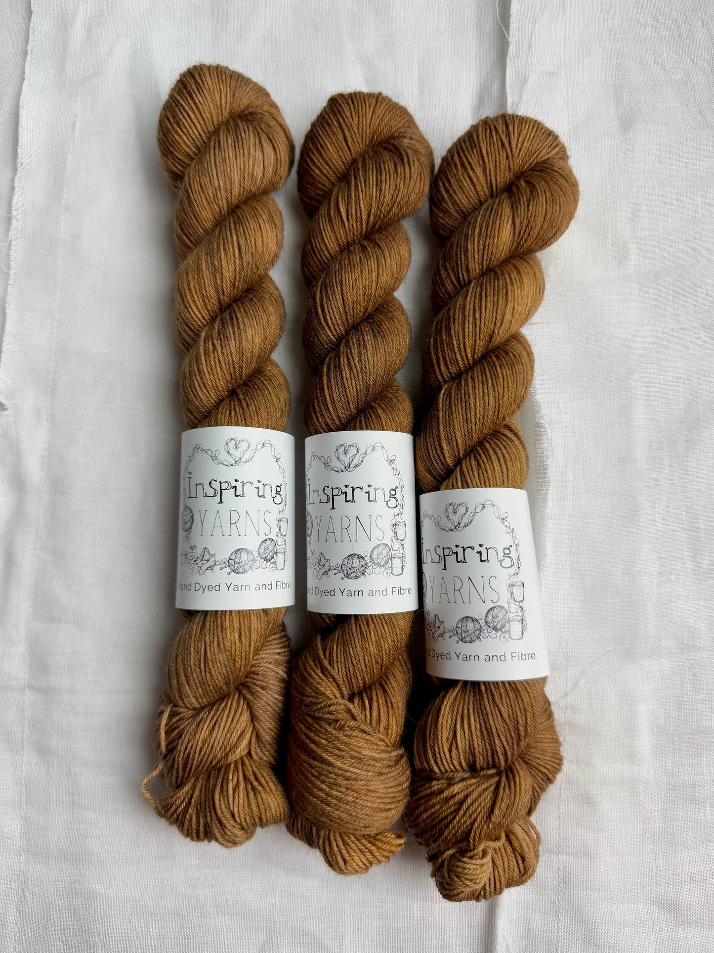 Three skeins of light brown tonal yarn with inspiring yans labels on a white background.