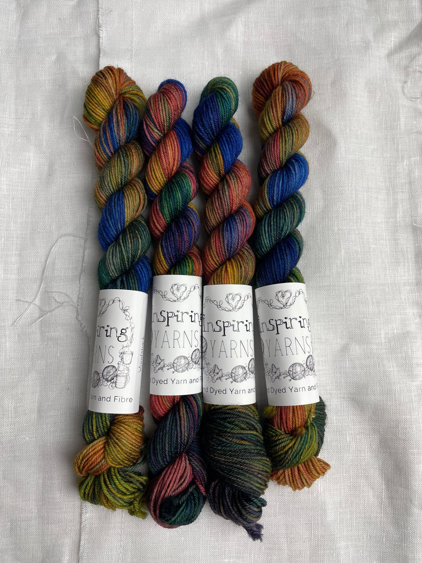 Four mini skeins of multi coloured Merino Smooth Sock yarn labelled Inspiring Yarns on a white linen background.