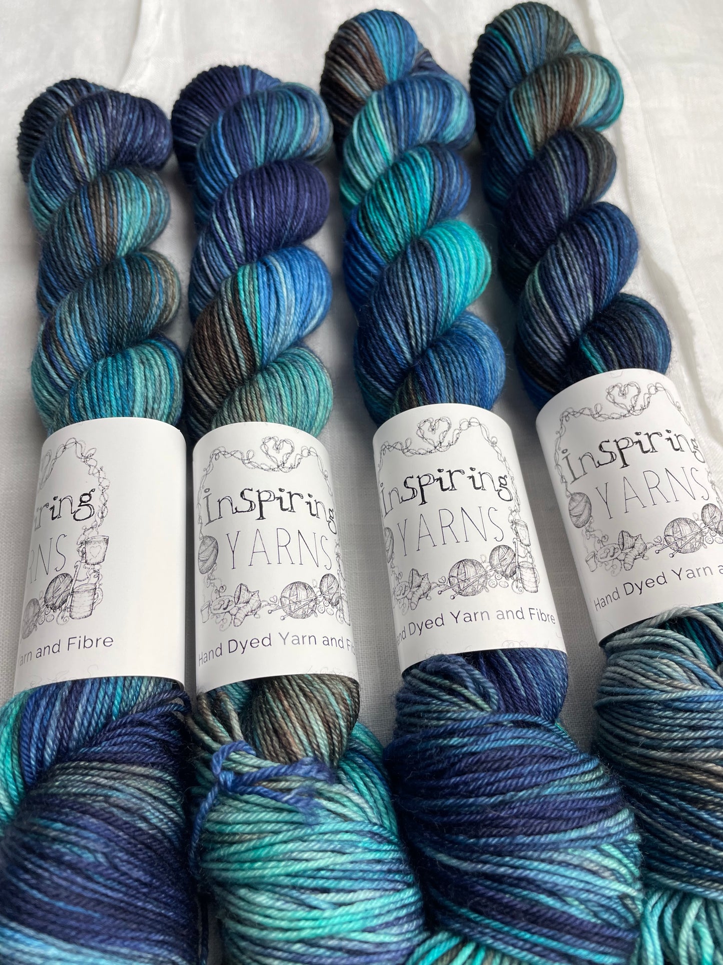 up close image of four skeins of yarn with black and white inspiring yarns labels on a plain white fabric background.