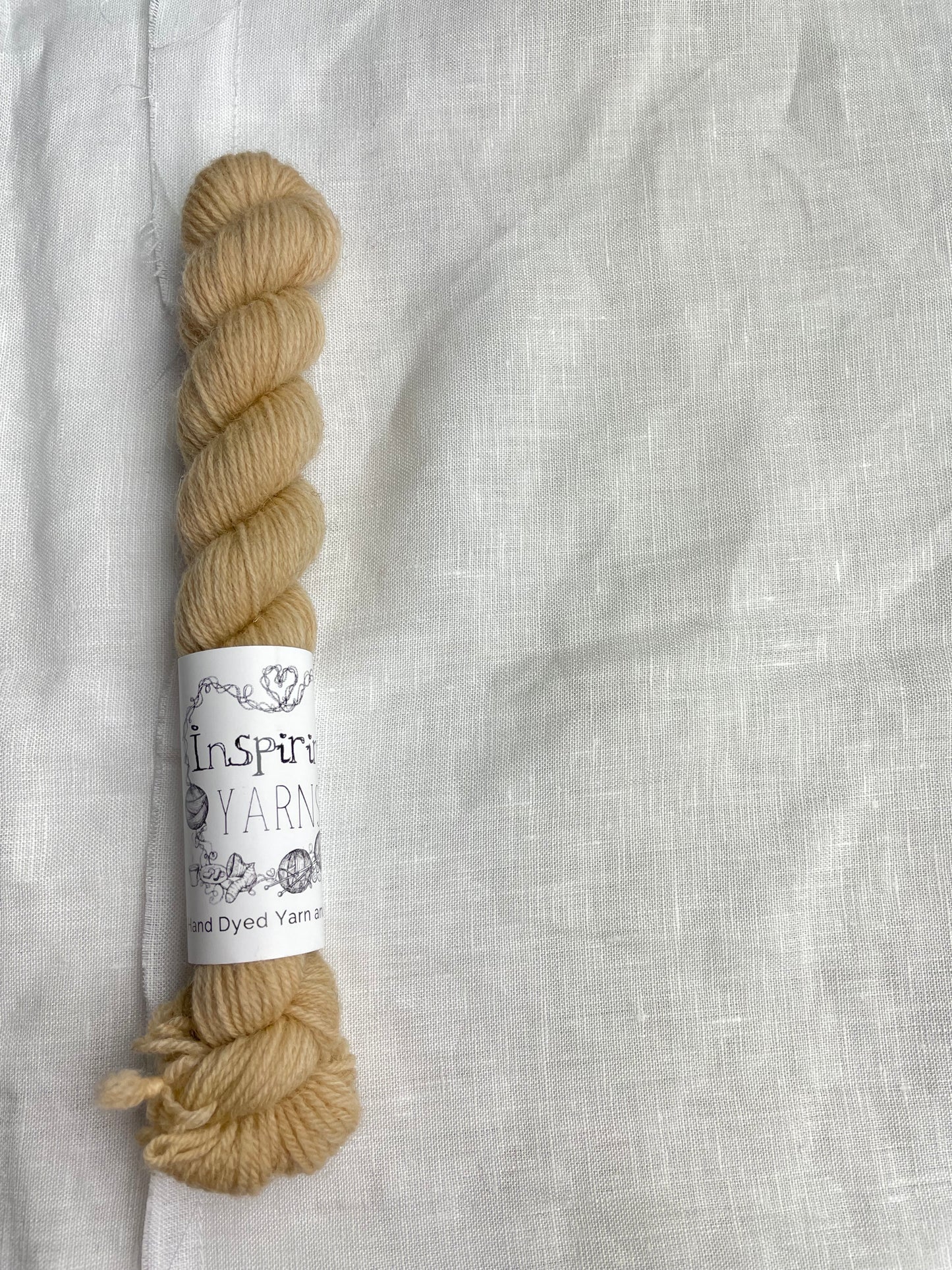 A mini skein of tonal golden caramel coloured Highland 4Ply yarn branded Inspiring Yarns on a white linen background.