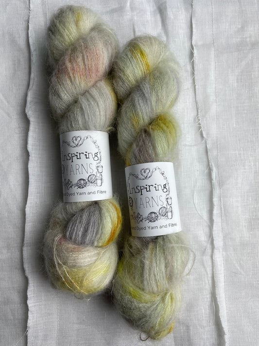 Two skeins of speckled  silver grey and mint coloured hand dyed fluffy Alpaca Silk Lace yarn labelled Inspiring Yarns on a white linen background.