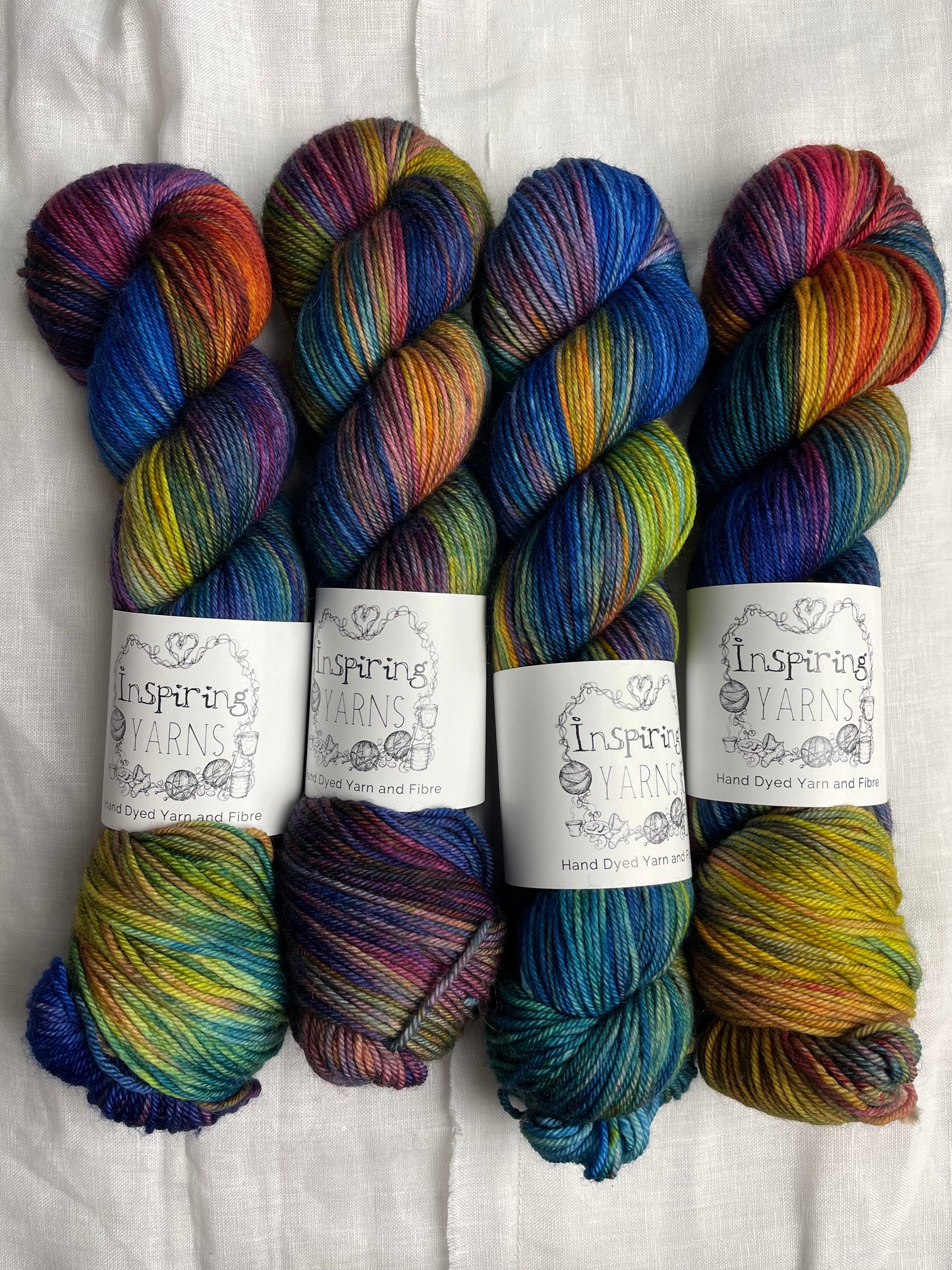 Four skeins of blue and multi coloured Merino Smooth DK yarn labelled Inspiring Yarns on a white linen background.