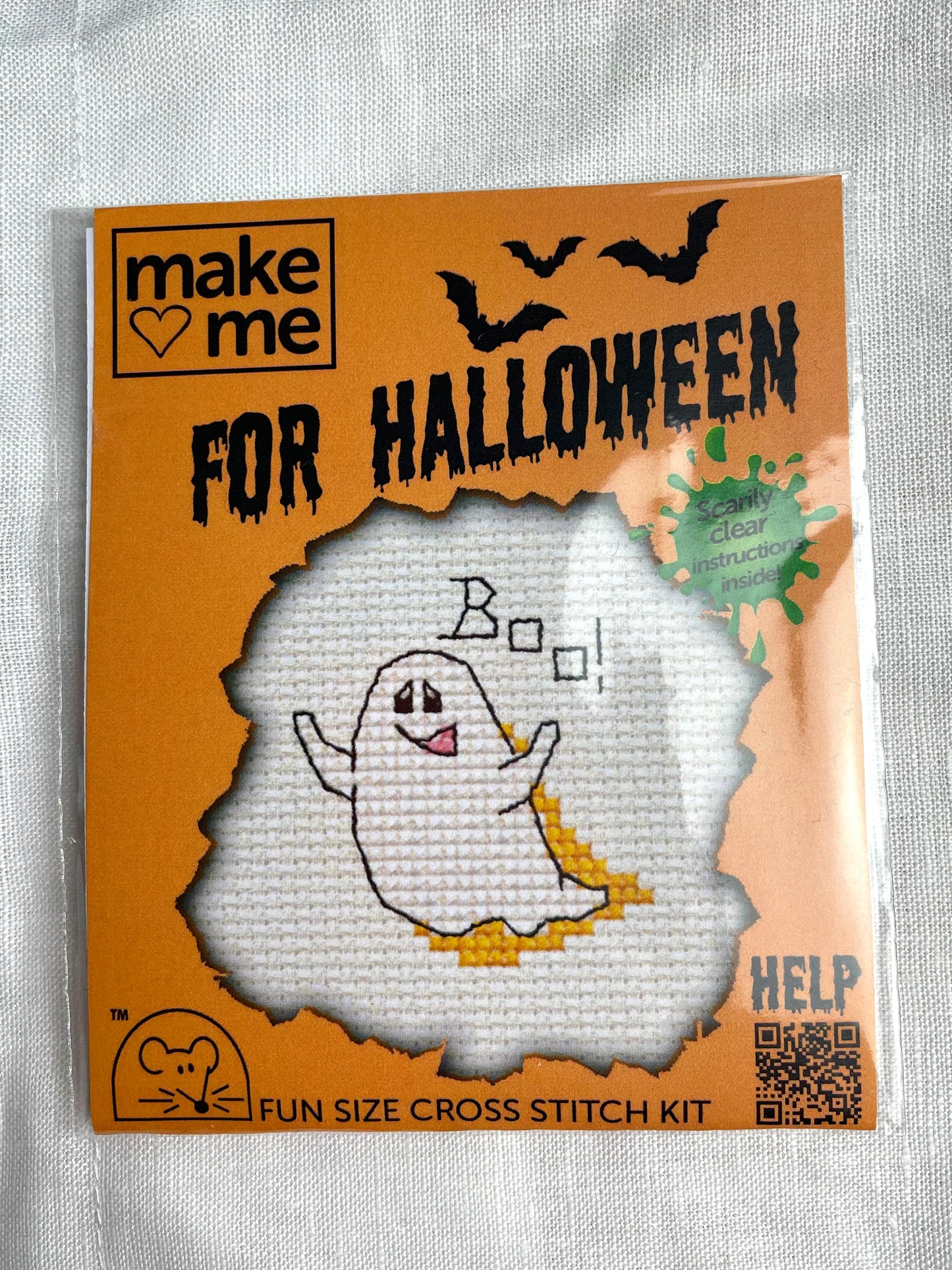 A mini crosstitch kit for a ghost saying boo photographed on a white linen background. It is branded Mouseloft Make Me For Halloween in orange packaging.