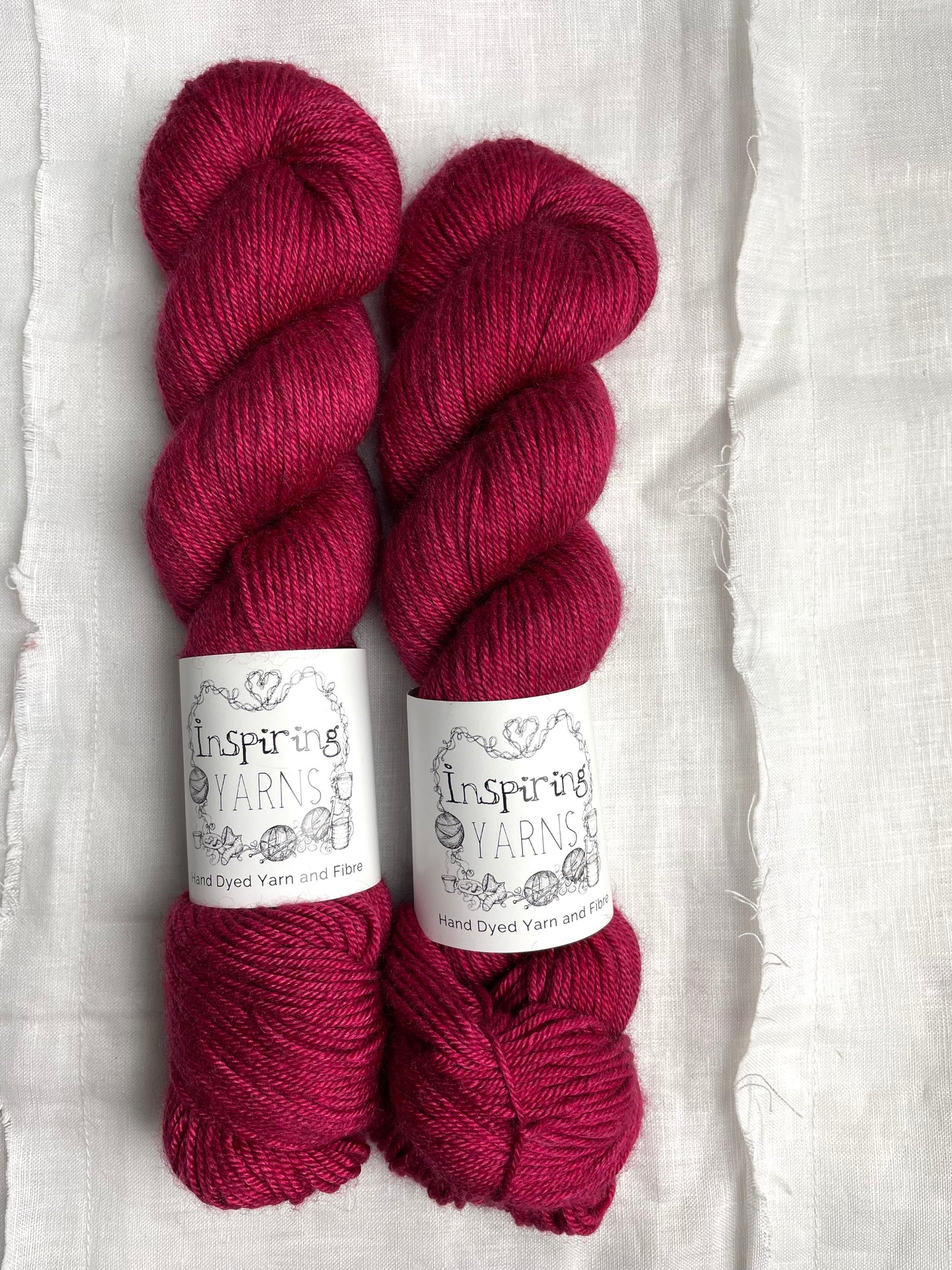 Two skeins of tonal bright cerise pink coloured yak silk dk yarn branded Inspiring Yarns on a white linen background.