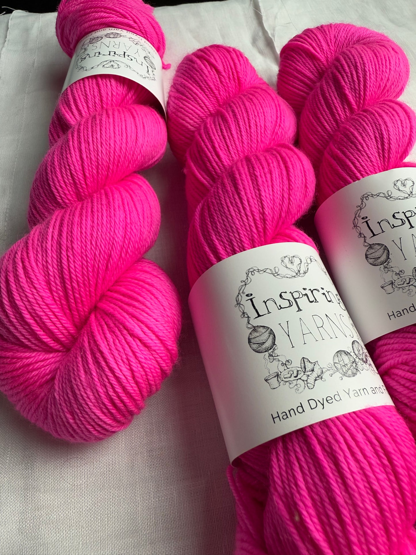 up close of three skeins of yarn in an intense neon pink with inspiring yarns label on a white background.