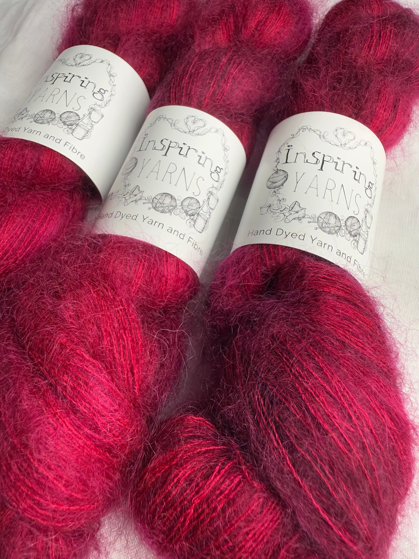 up close of fluffy mohair in dark ruby red with white background and inspiring yarns labels.