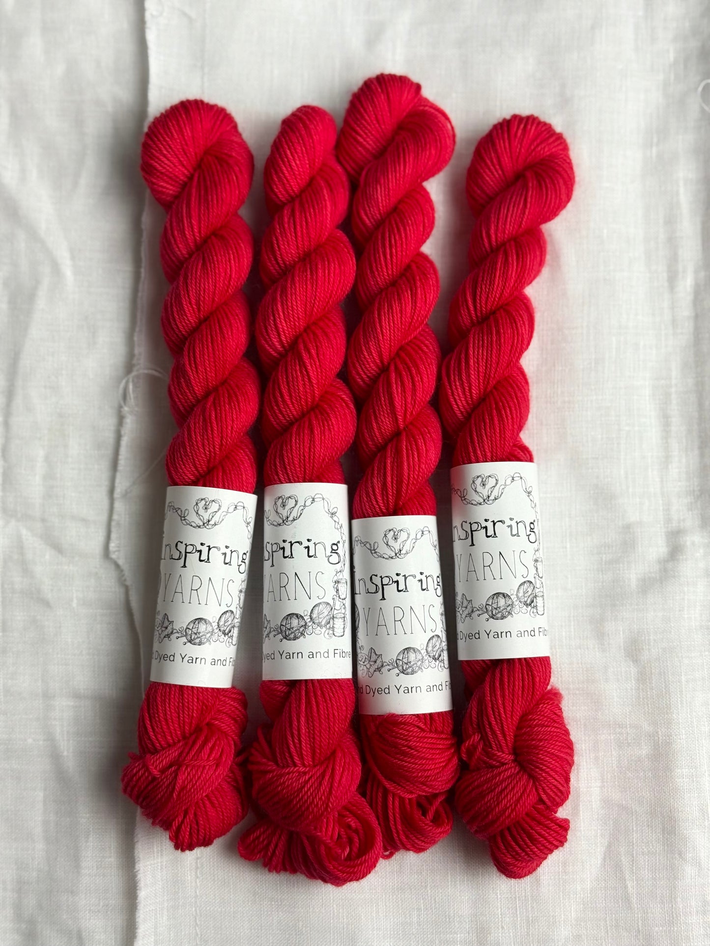 Four skeins of bright coral red merino wool yarn with Inspiring Yarns labels on a white fabric background.