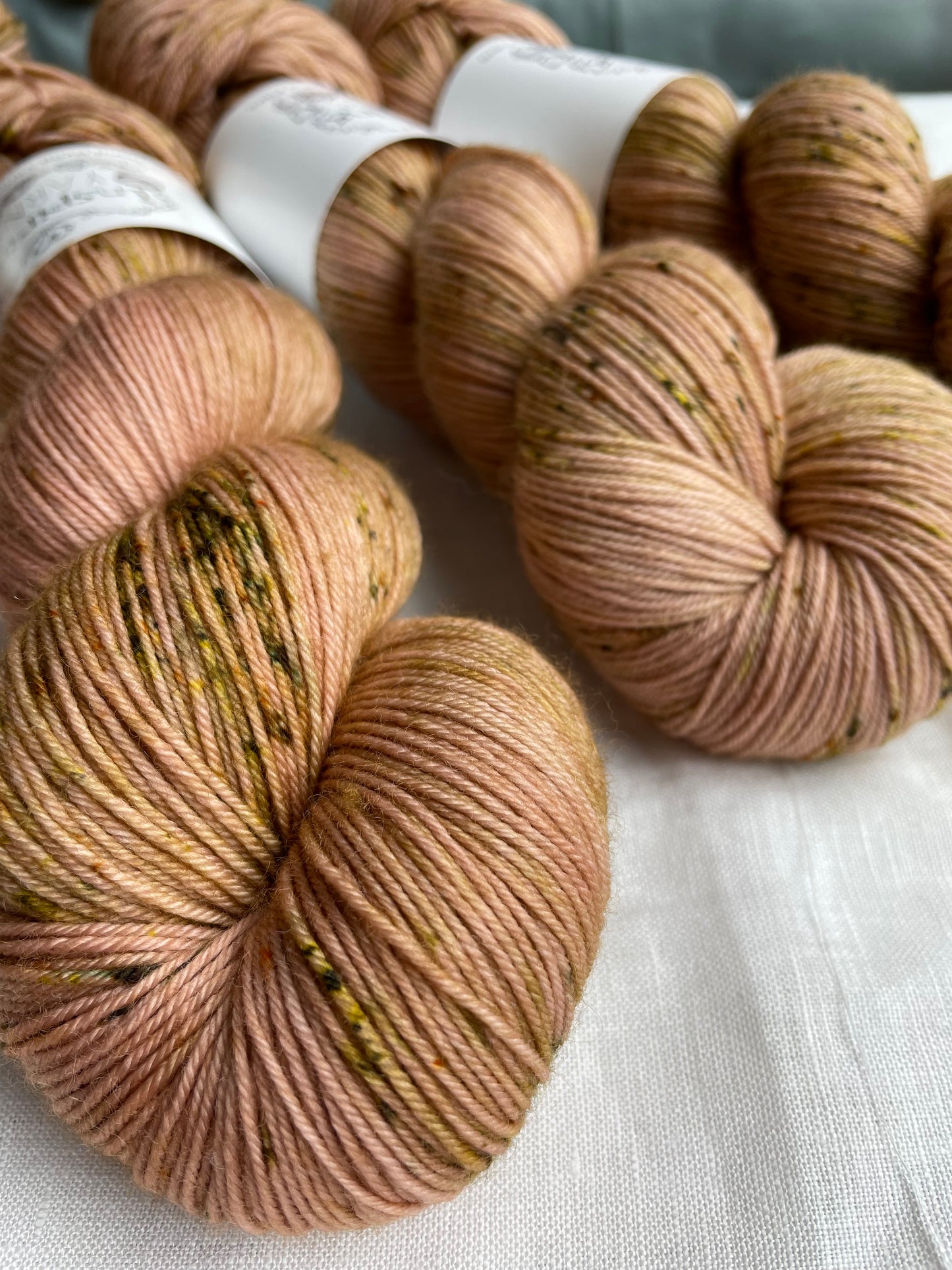Close up of four speckled soft terracotta coloured skeins of Merino Smooth Sock yarn branded Inspiring Yarns on a white linen fabric background.