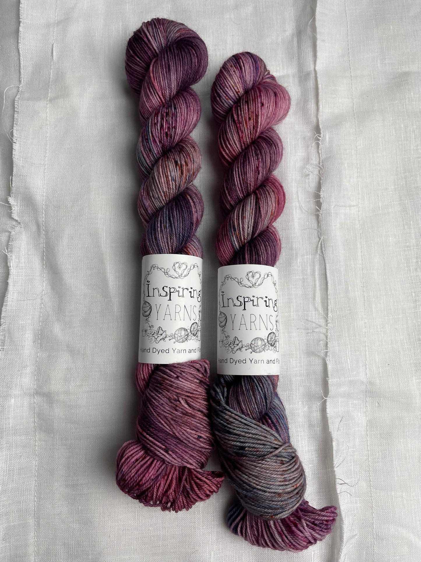 Two skeins of merino smooth sock in shades of pink and blue labelled Inspiring Yarns on a white linen background.