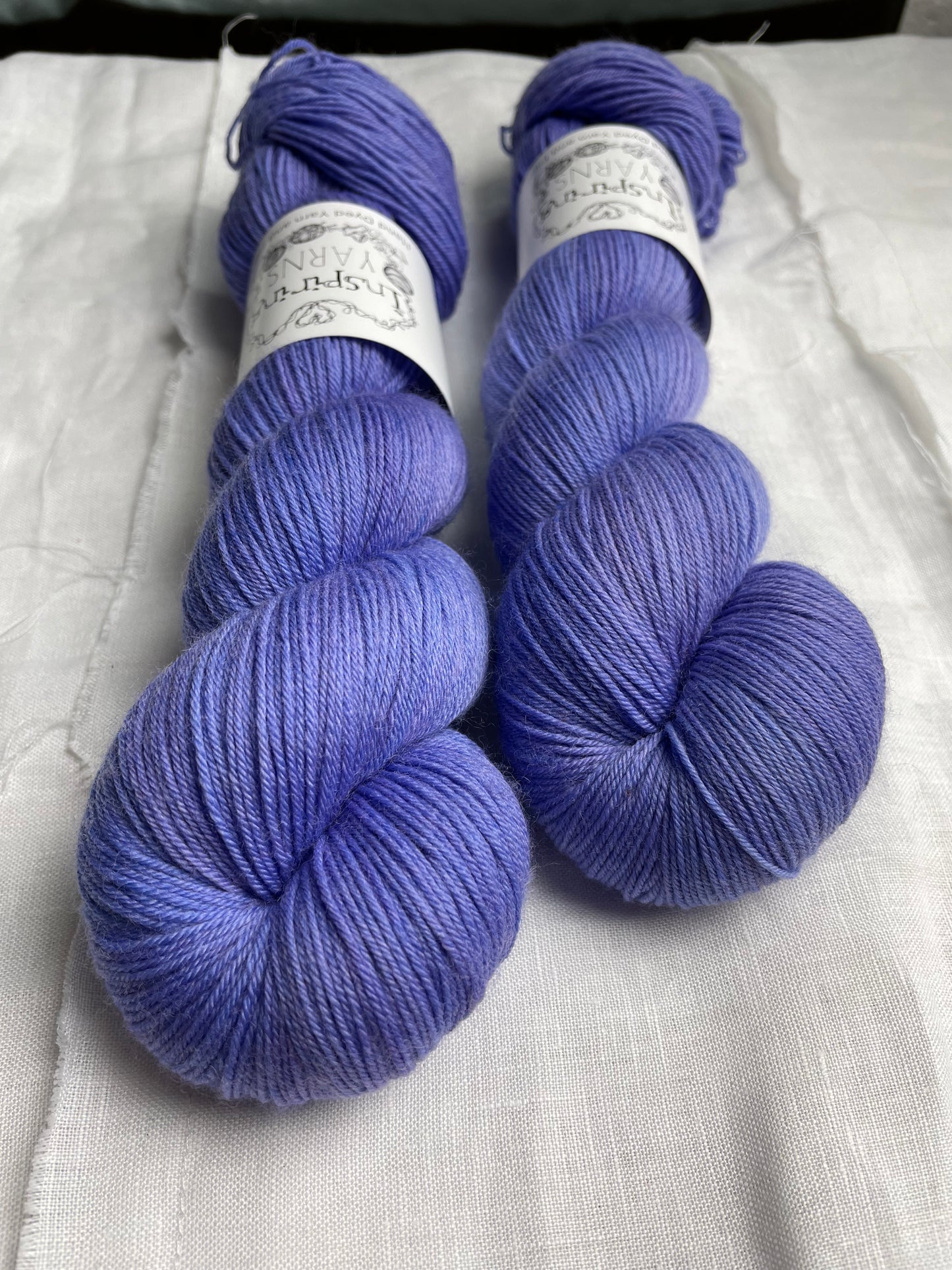 Two skeins of Moonstone, blue lilac coloured Merino Smooth Sock labelled Inspiring Yarns on a white linen background.