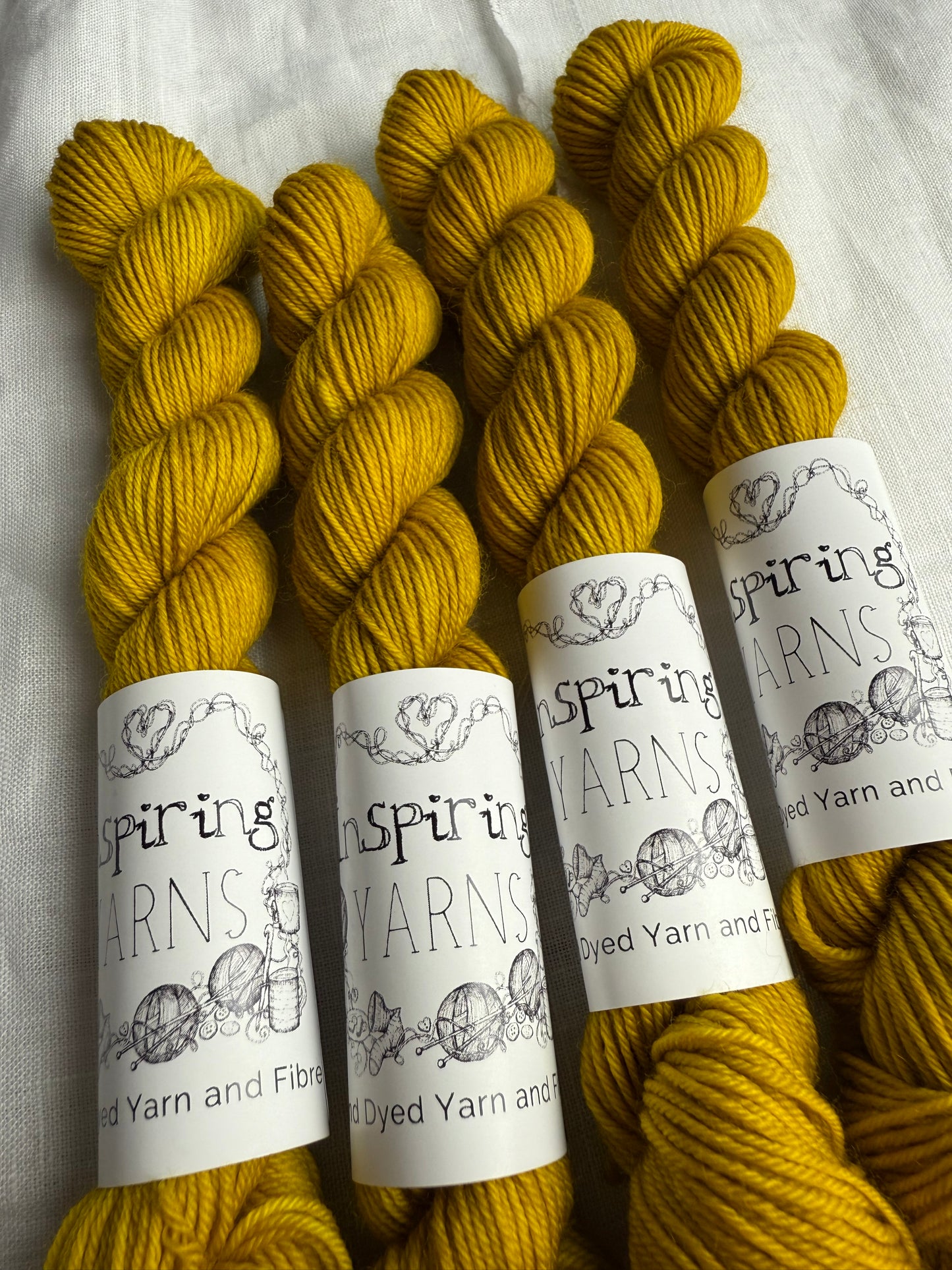 up close of four tonal yellow skeins of yarn. with inspiring yarns labels in black and white on plain white fabric background.