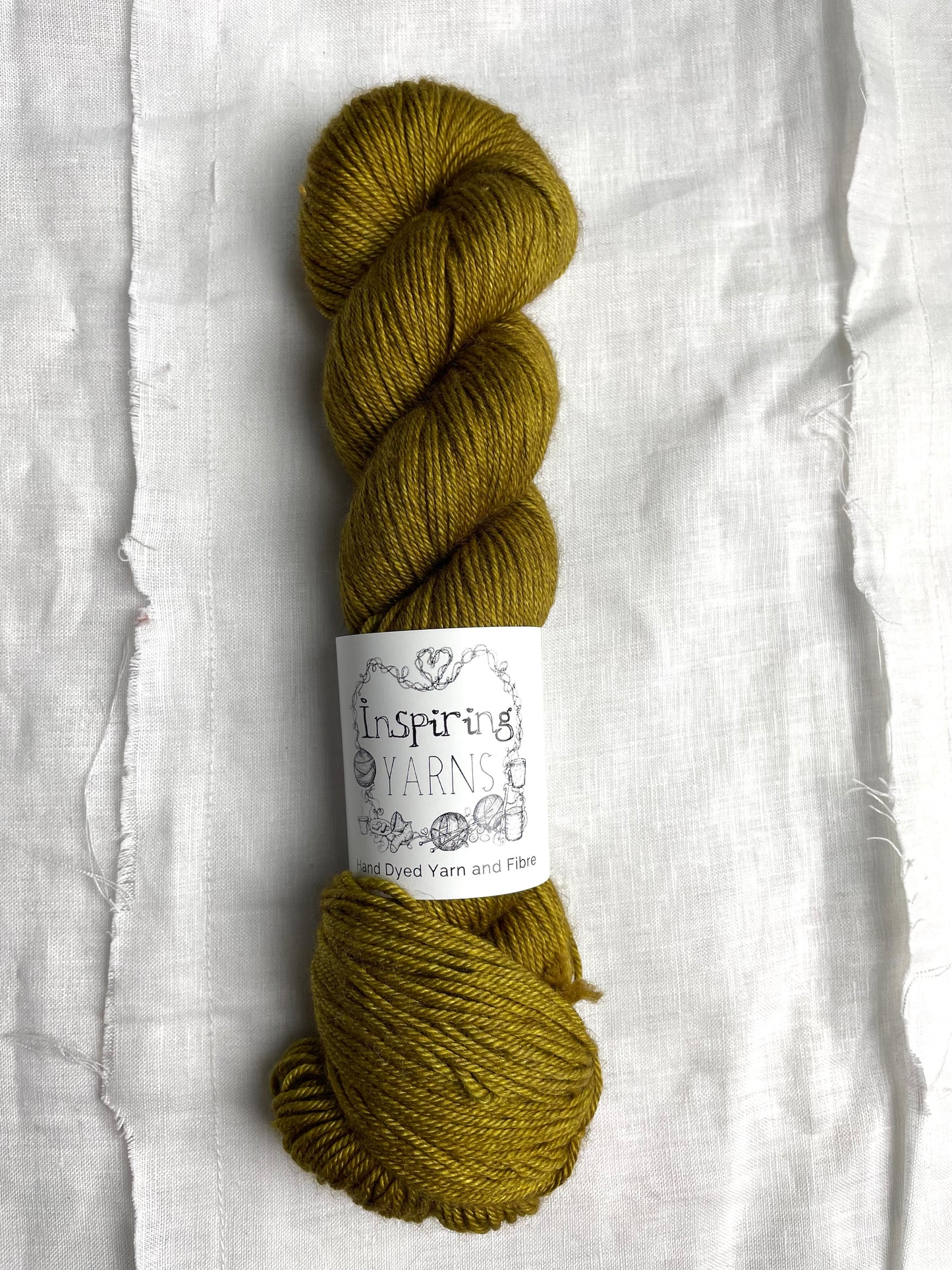 One skein of ochre coloured yak silk dk yarn branded Inspiring Yarns on a white linen background.