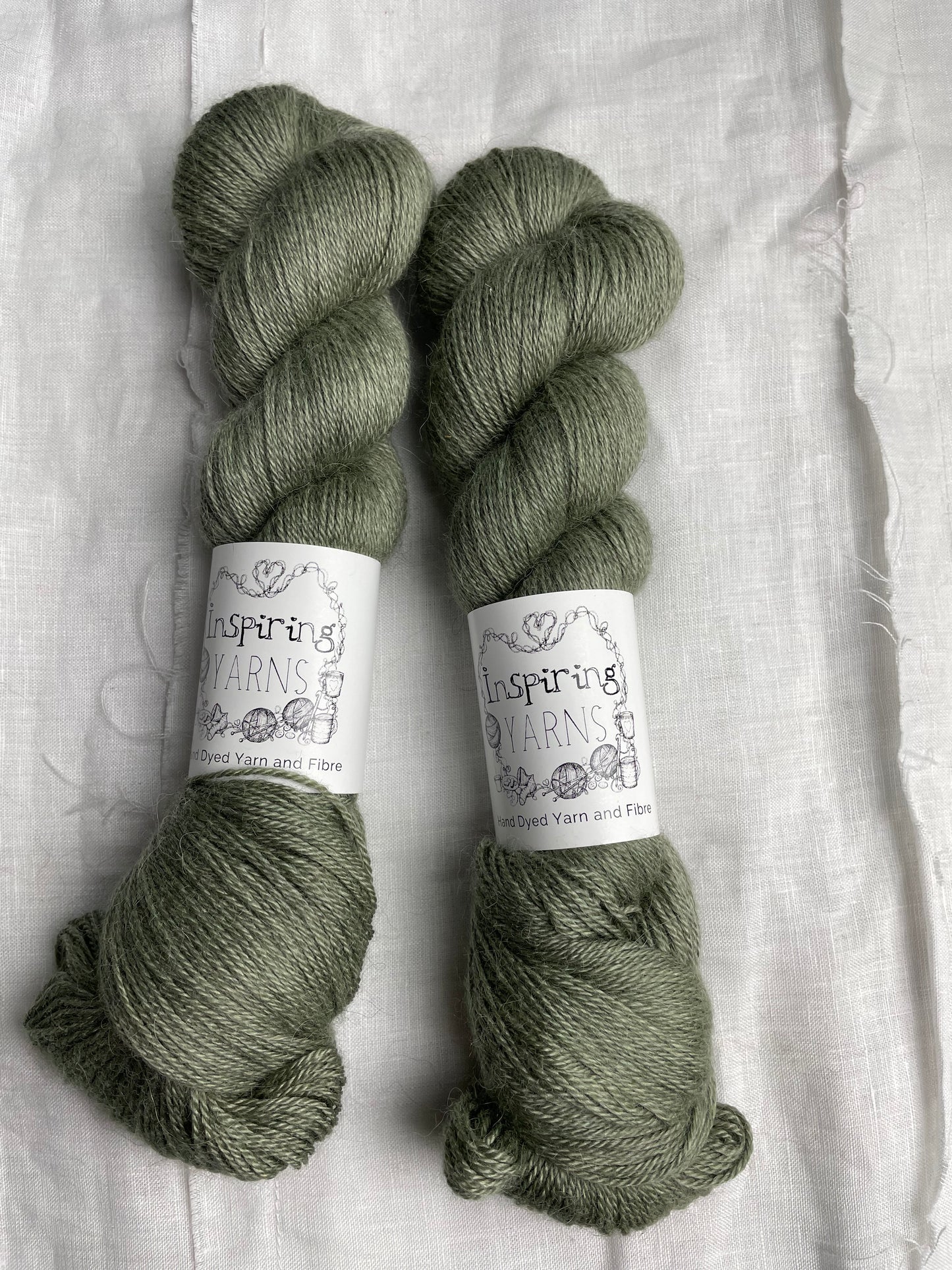 Two skeins of pale green mist 4ply yarn labelled Inspiring Yarns on a white linen background.
