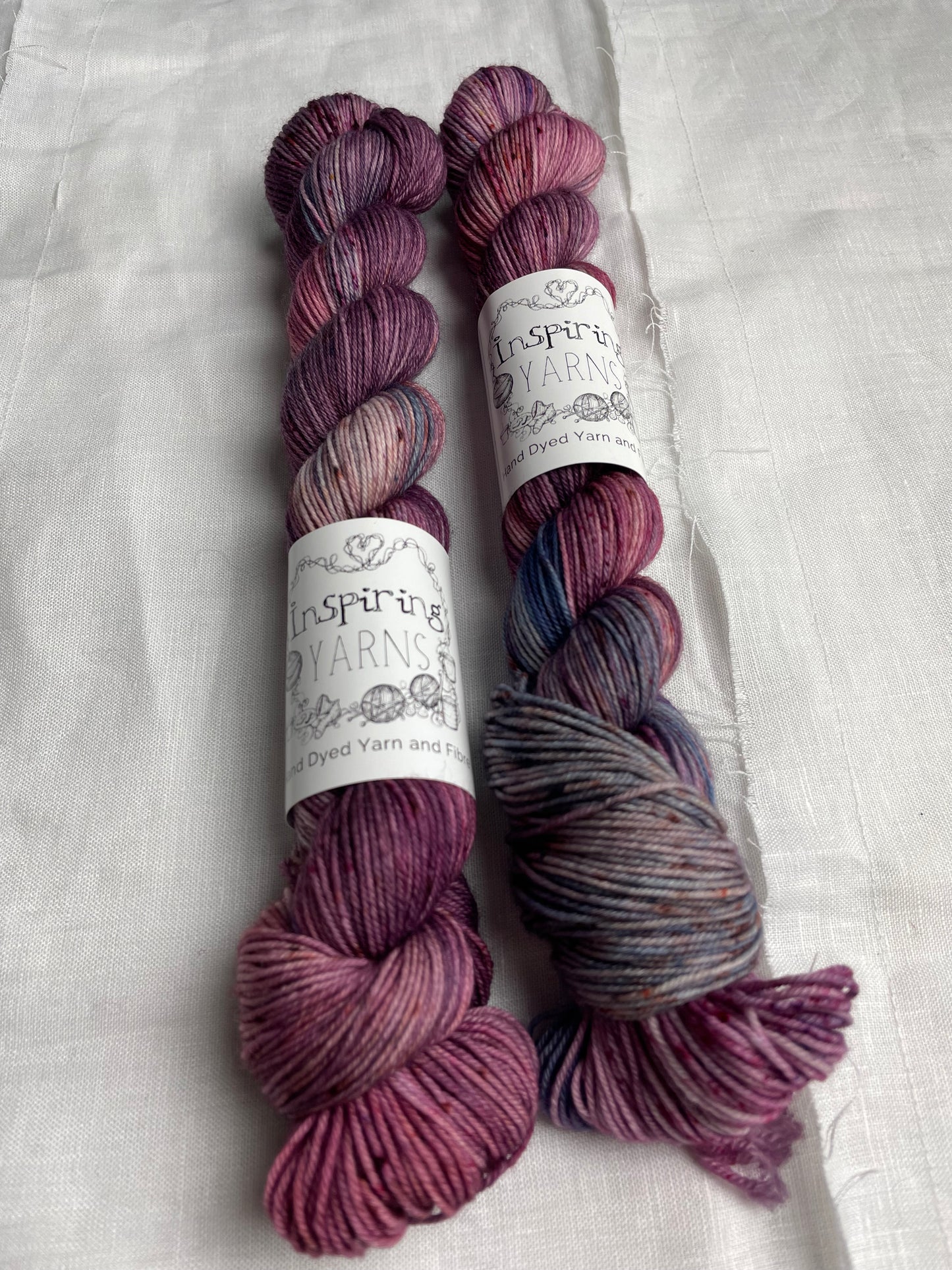 Two skeins of merino smooth sock in shades of pink and blue labelled Inspiring Yarns on a white linen background.