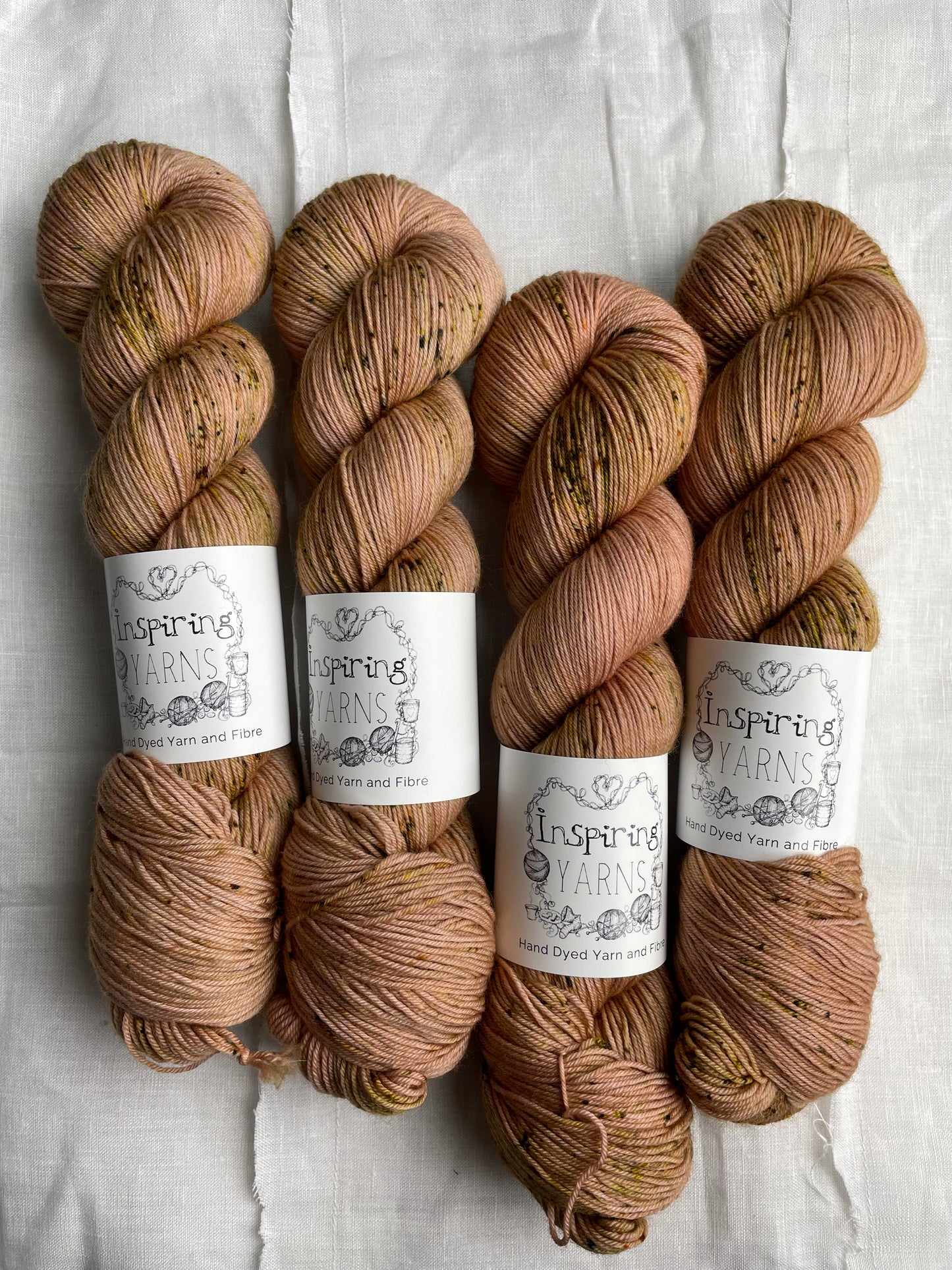 Four speckled soft terracotta coloured skeins of Merino Smooth Sock yarn branded Inspiring Yarns on a white linen fabric background.
