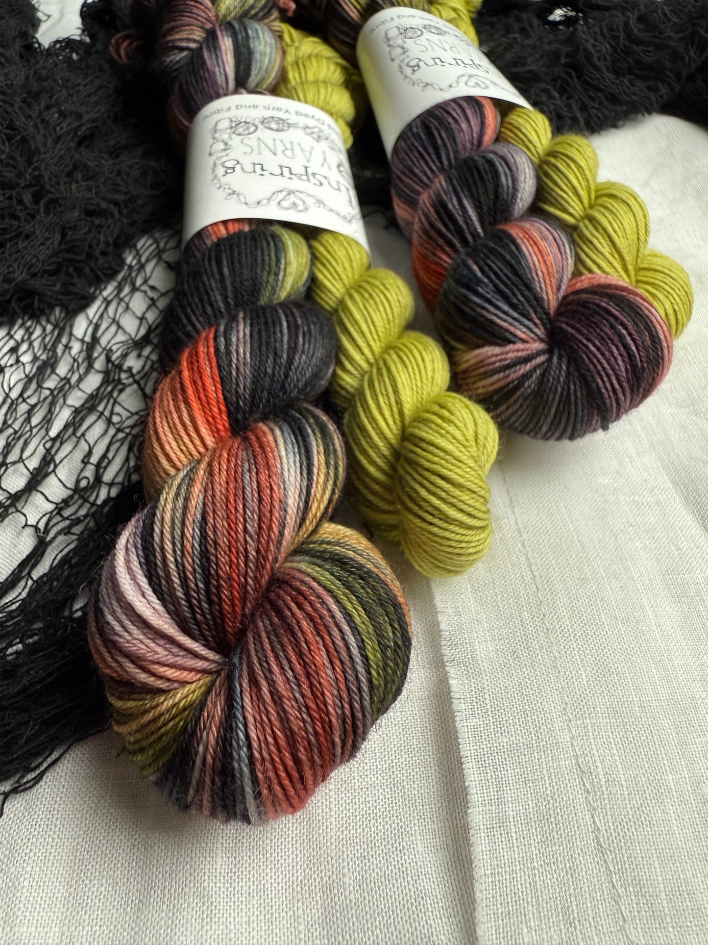 up close of two yarn sock sets, one skin is black with flashes of green, orange and lilac the other is a mini skein in a lime green