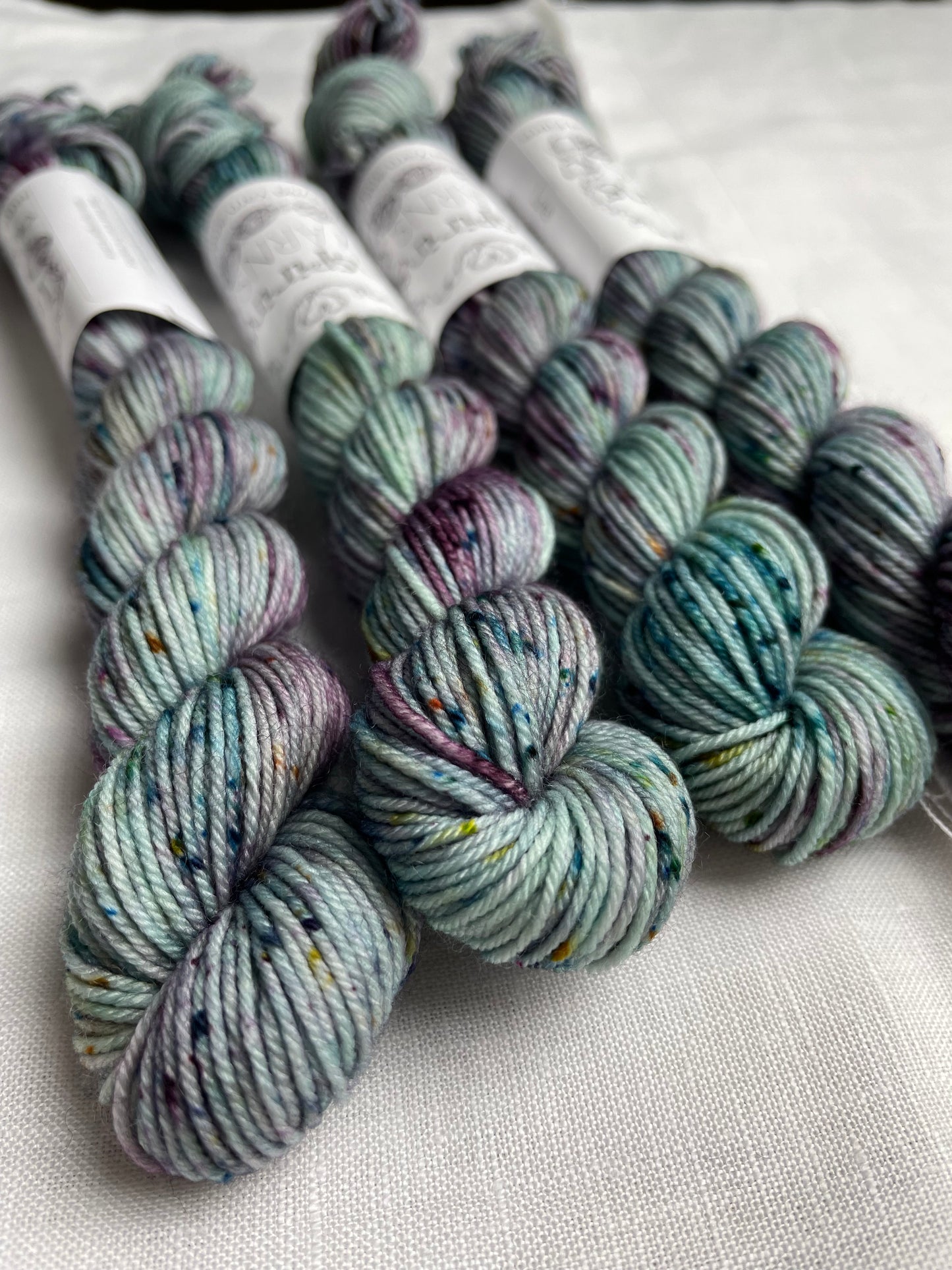 Four skeins of merino smooth sock yarn in a light teal colour with coloured speckles labelled Inspiring Yarns on a white linen background.