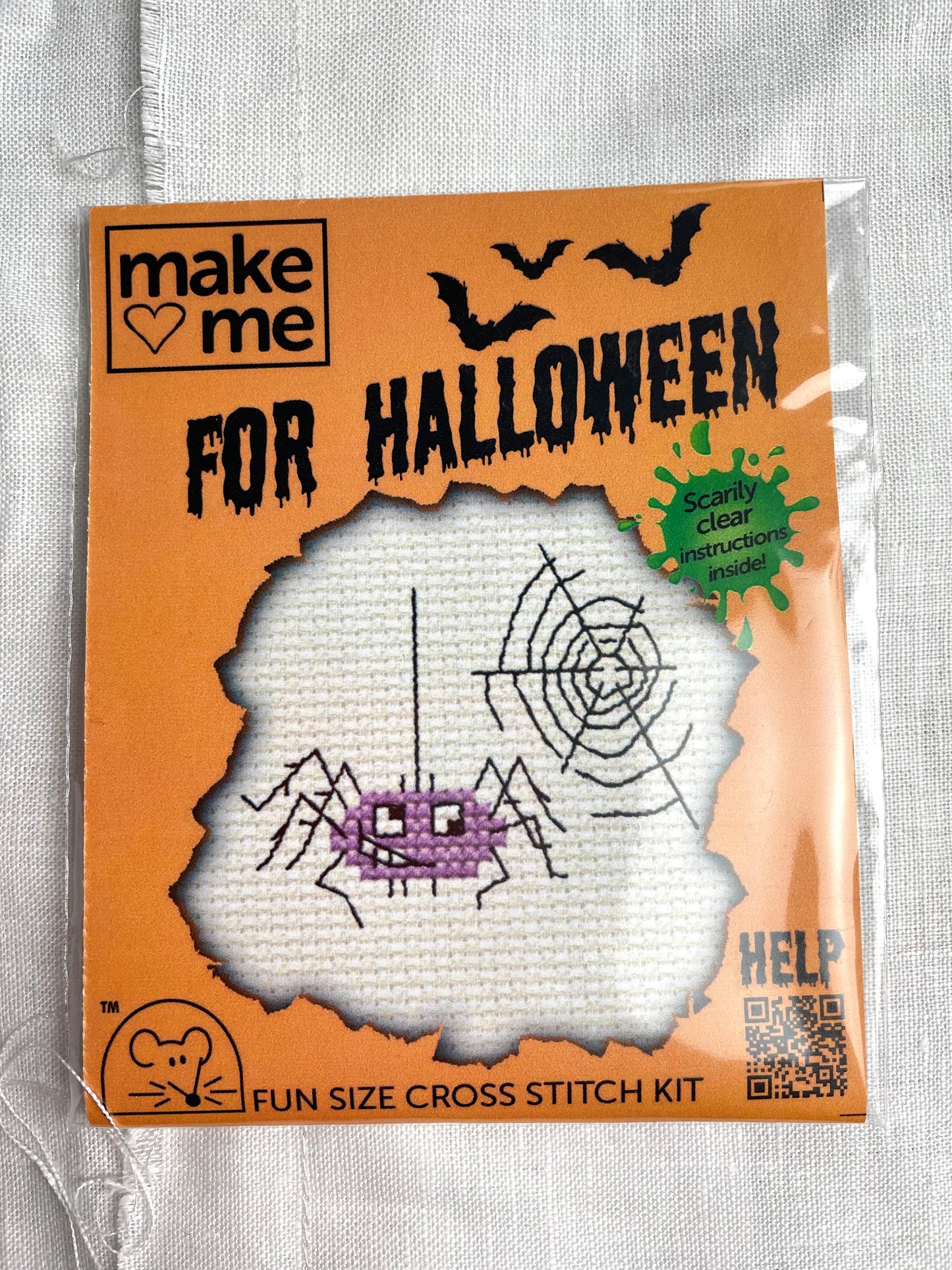 A mini crosstitch kit for a purple spider and a web photographed on a white linen background. It is branded Mouseloft Make Me For Halloween in orange packaging.
