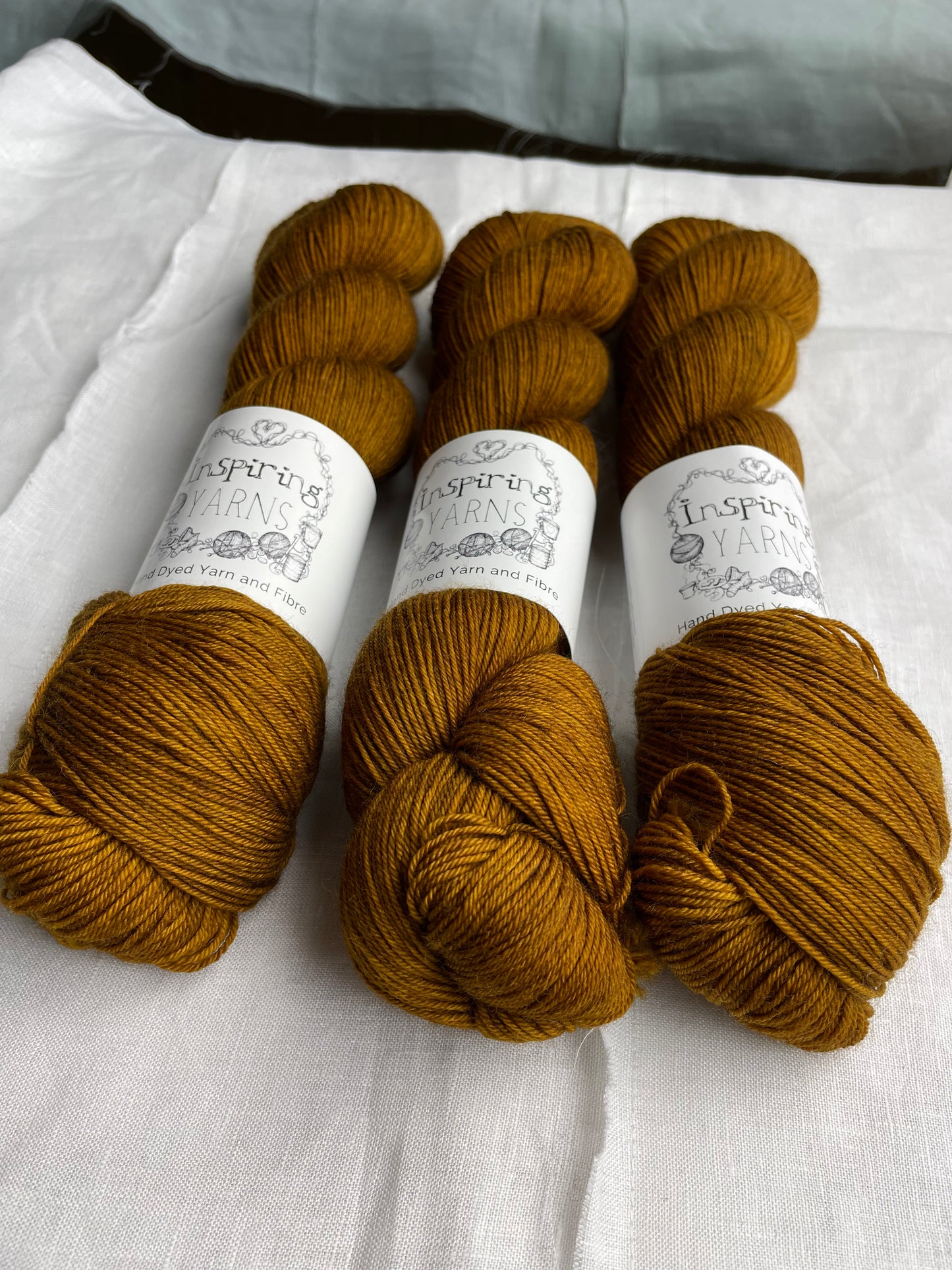 Three tonal toffee brown coloured skeins of Merino Smooth Sock yarn branded Inspiring Yarns on a white linen fabric background.
