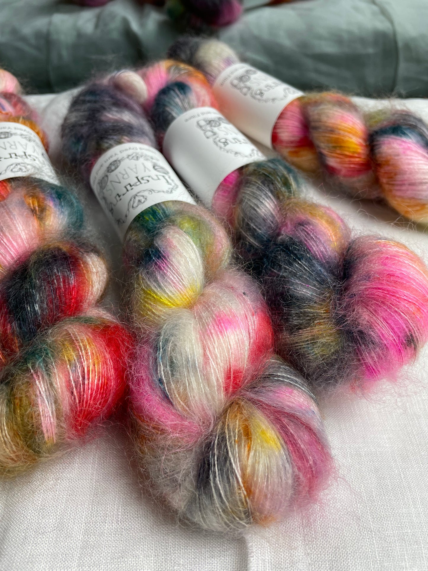 Four skeins of multi coloured speckled kid mohair silk lace yarn labelled Inspiring Yarns on a white linen background.