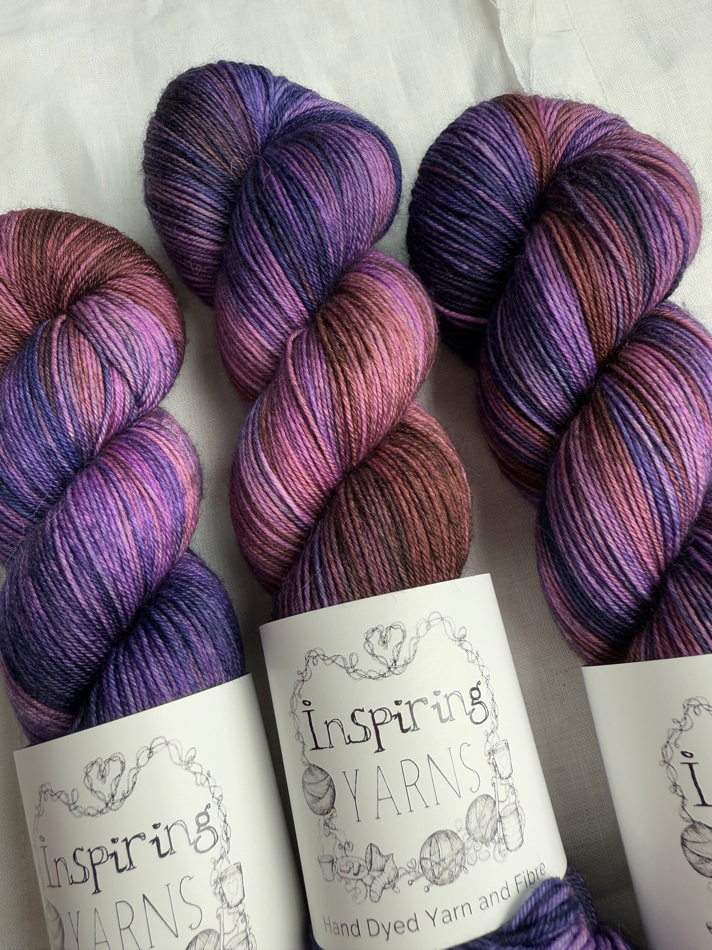 up close skeins of variegated yarn with purples, violets and browns. on white background and inspiring yarns label.