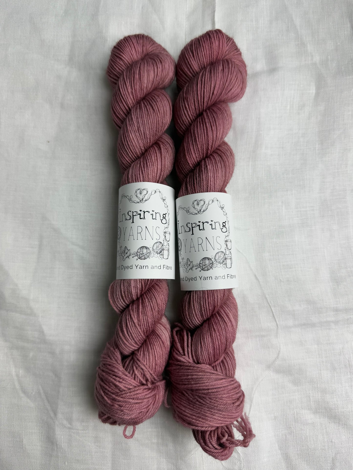 two skeins of dusty pink hand dyed yarn side by side on what background with inspiring yarns labels.