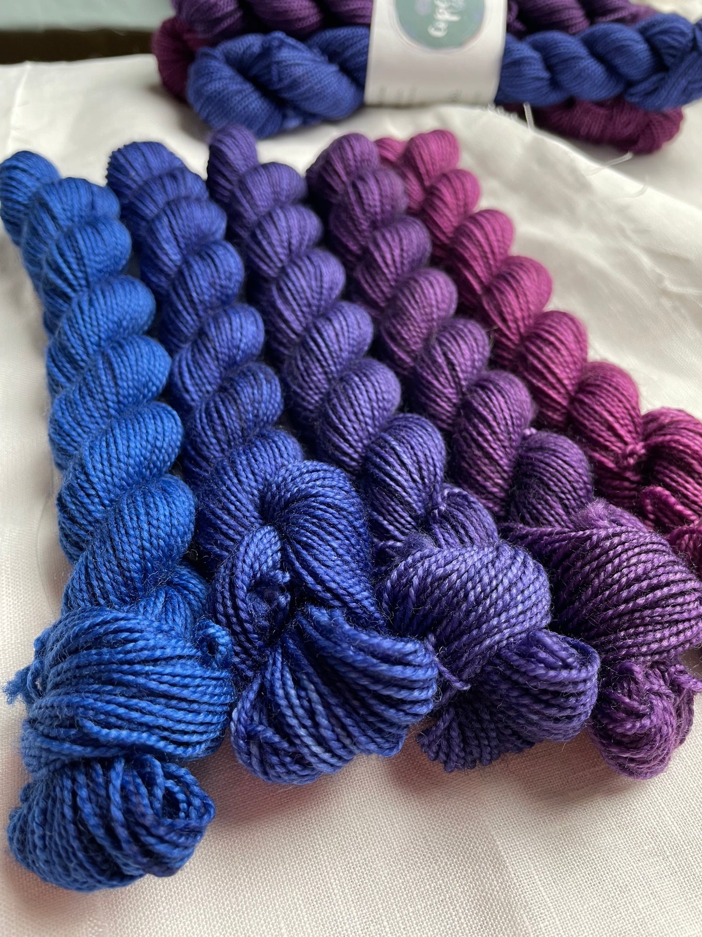 Close up of 2 sets of 5 mini skeins in a blue to purple fade by Copeland Yarns on a white background