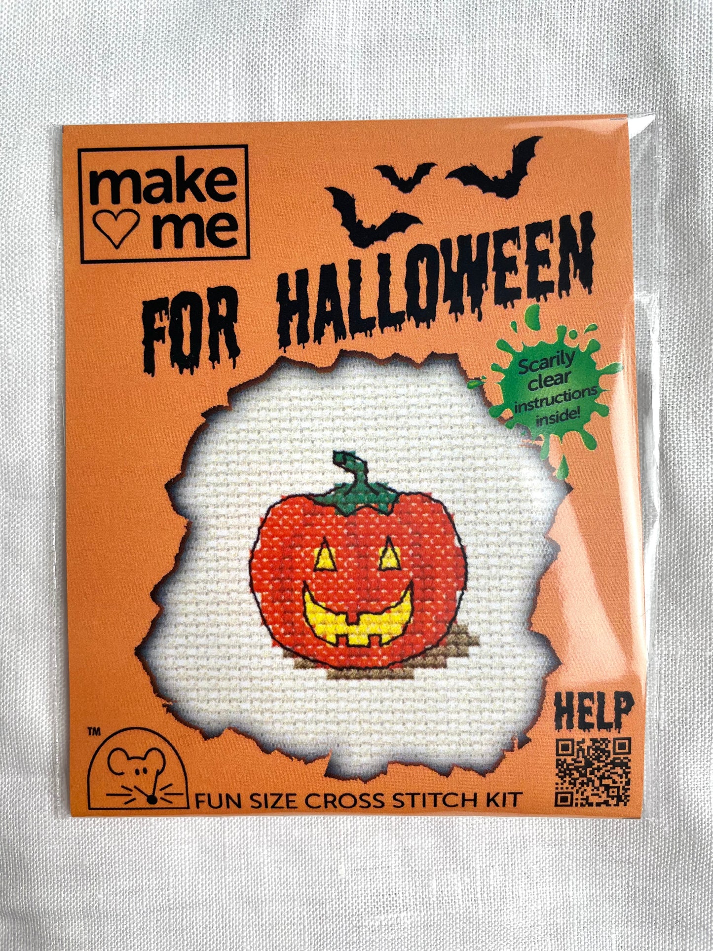 A mini crosstitch kit for a pumpkin lantern photographed on a white linen background. It is branded Mouseloft Make Me For Halloween in orange packaging.
