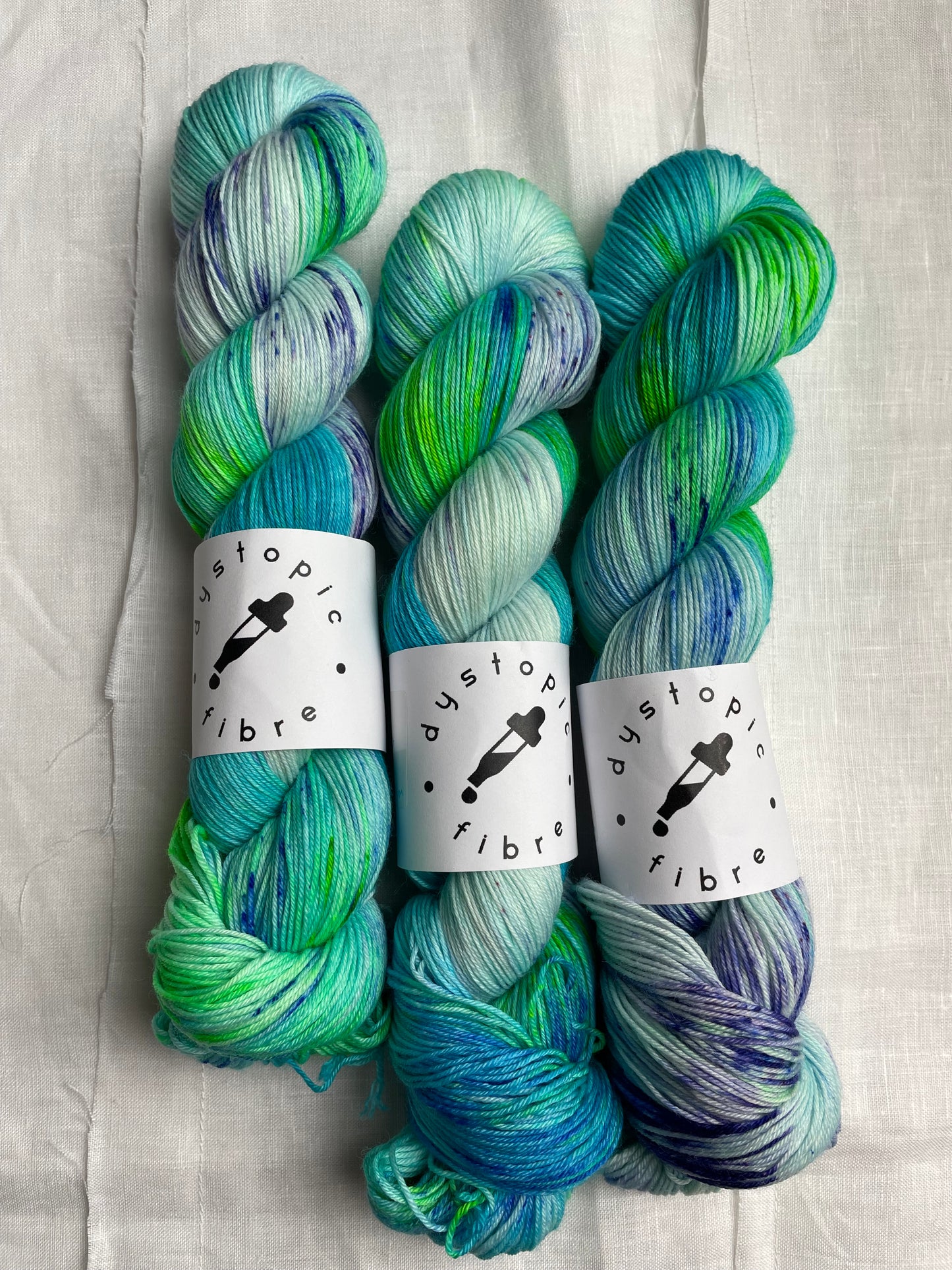 3 skeins of turquoise and green hand dyed yarn by Dystopic Fibre on a white background
