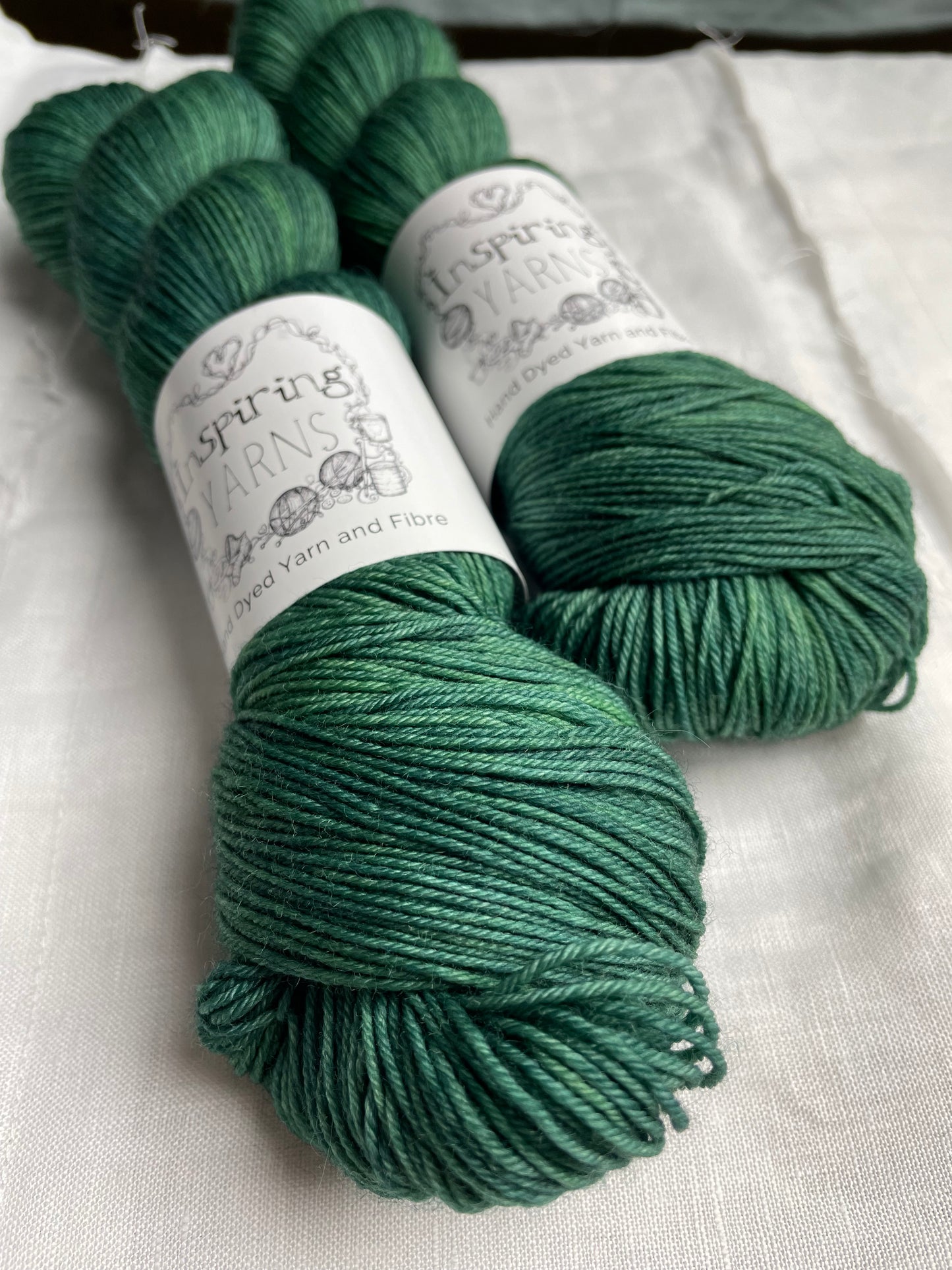 Two skeins of merino smooth sock yarn in a tonal light green blue colour labelled Inspiring Yarns on a white linen background.