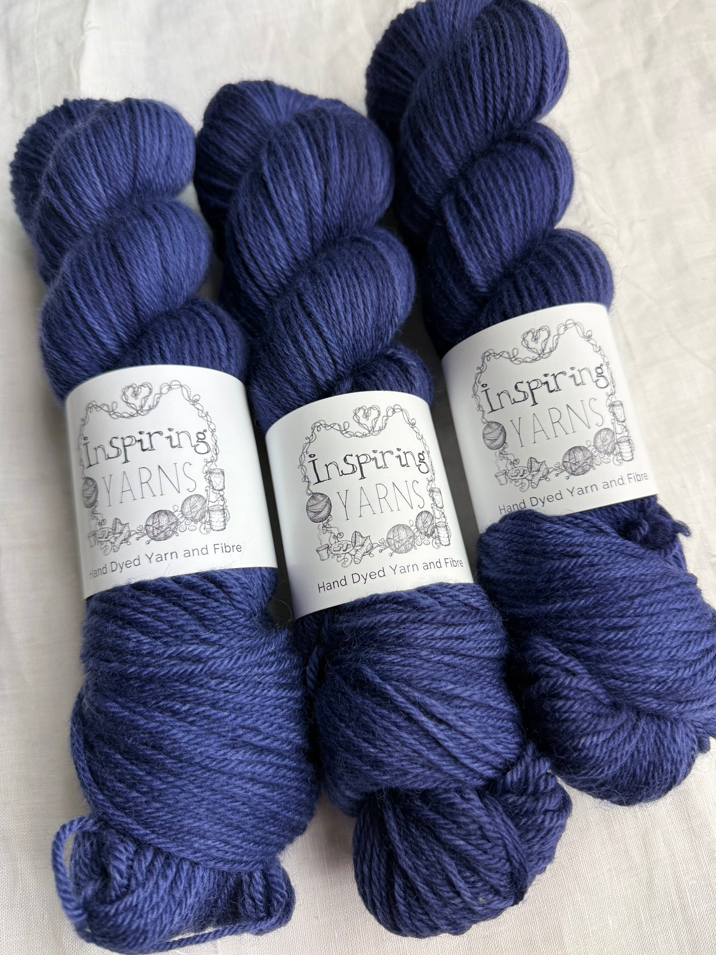 Three skeins of dark navy tonal yarn labelled Inspiring Yarns on a white background