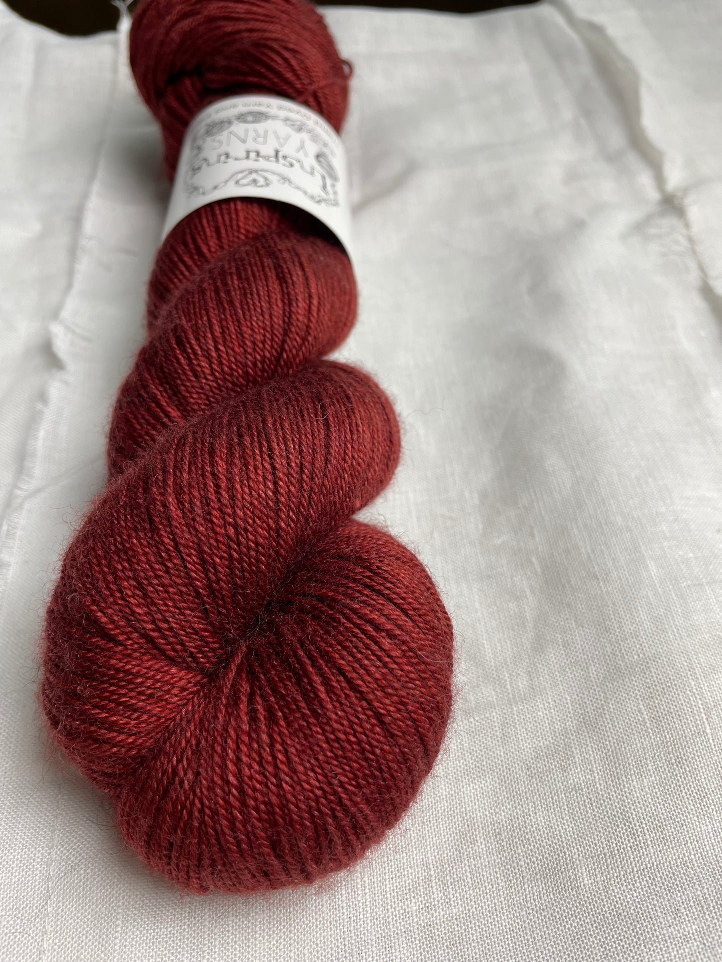A skein of rust red Yak Silk 4ply yarn labelled Inspiring Yarns on a white linen background.
