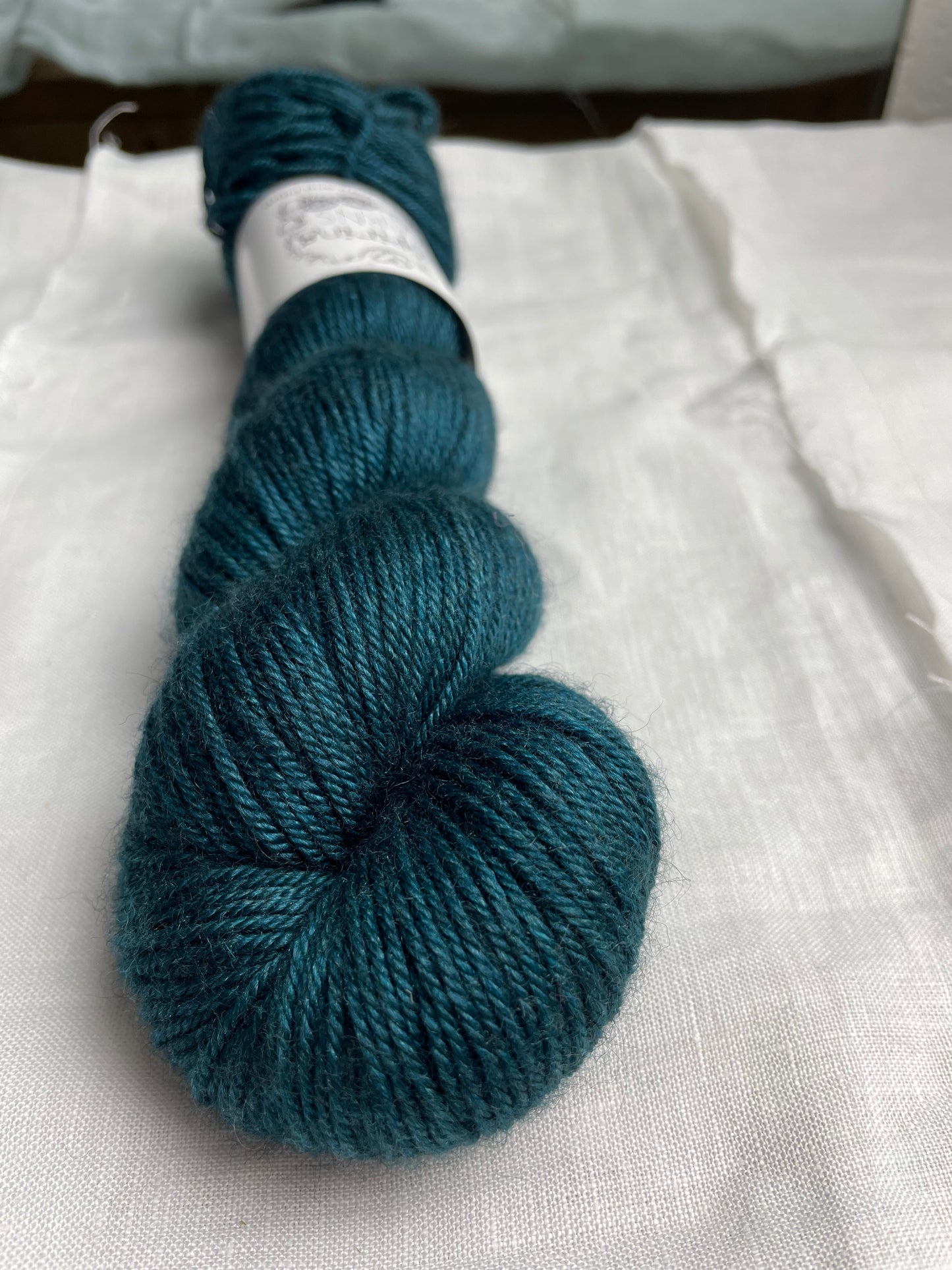 One skein of teal blue coloured yak silk dk yarn branded Inspiring Yarns on a white linen background.