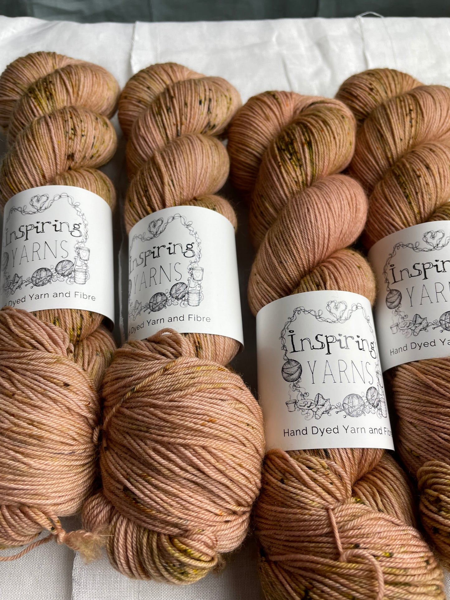 Four speckled soft terracotta coloured skeins of Merino Smooth Sock yarn branded Inspiring Yarns on a white linen fabric background.