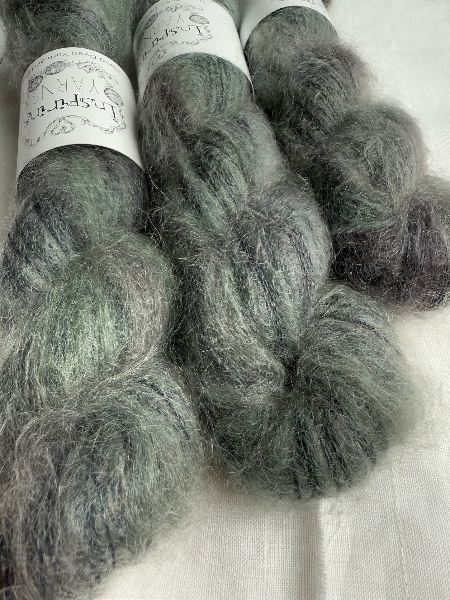 three skeins of grey yarn with green tones with white inspiring yarns labels on white background.