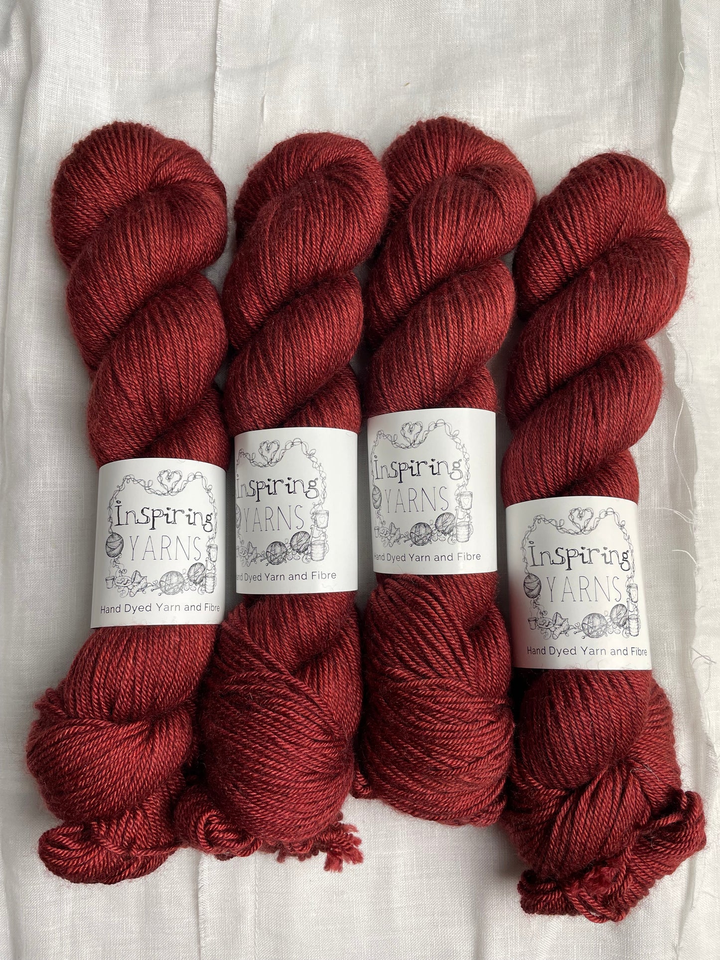 Four skeins of rusty red coloured yak silk dk yarn branded Inspiring Yarns on a white linen background.