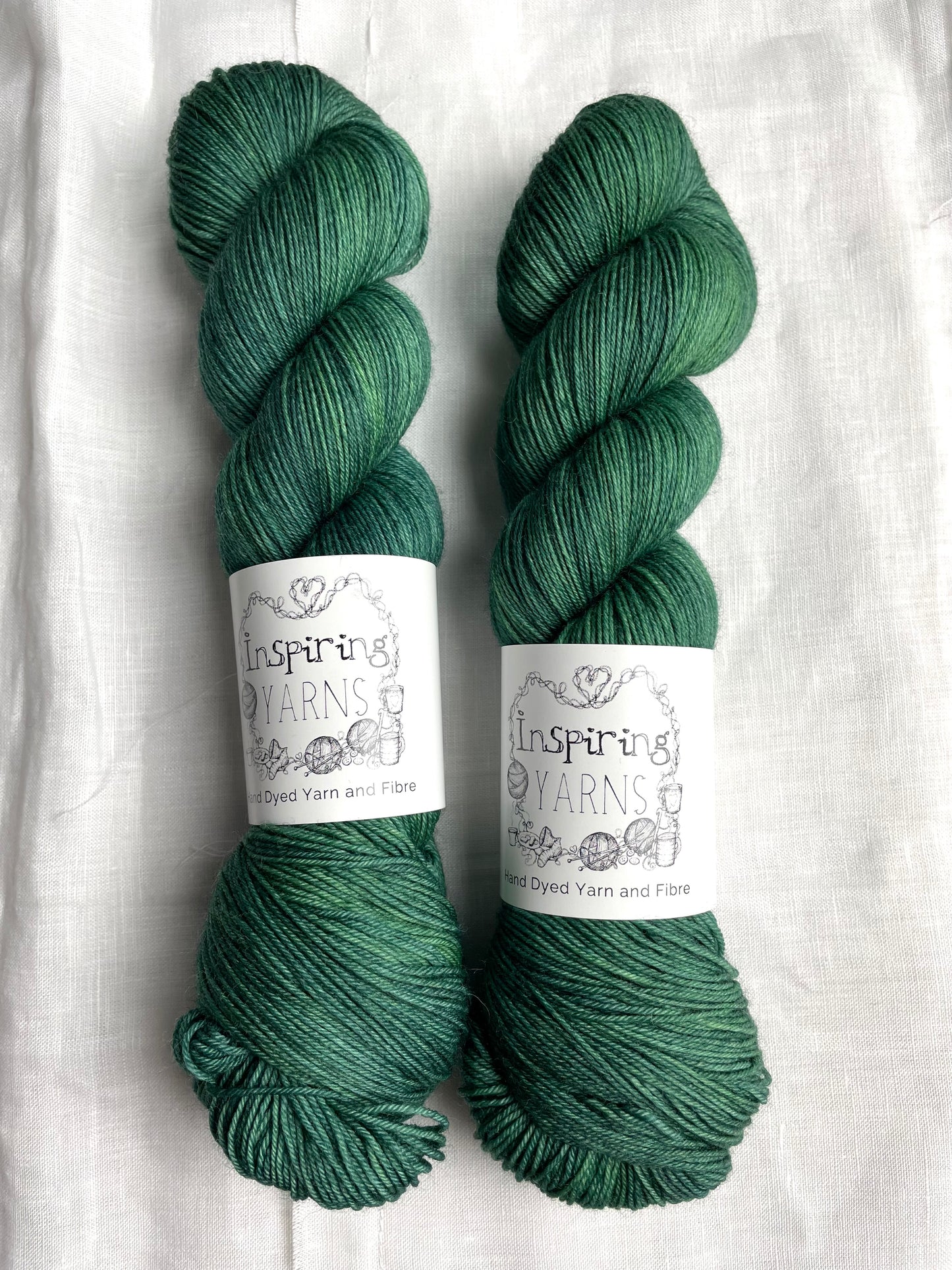 Two skeins of merino smooth sock yarn in a tonal light green blue colour labelled Inspiring Yarns on a white linen background.