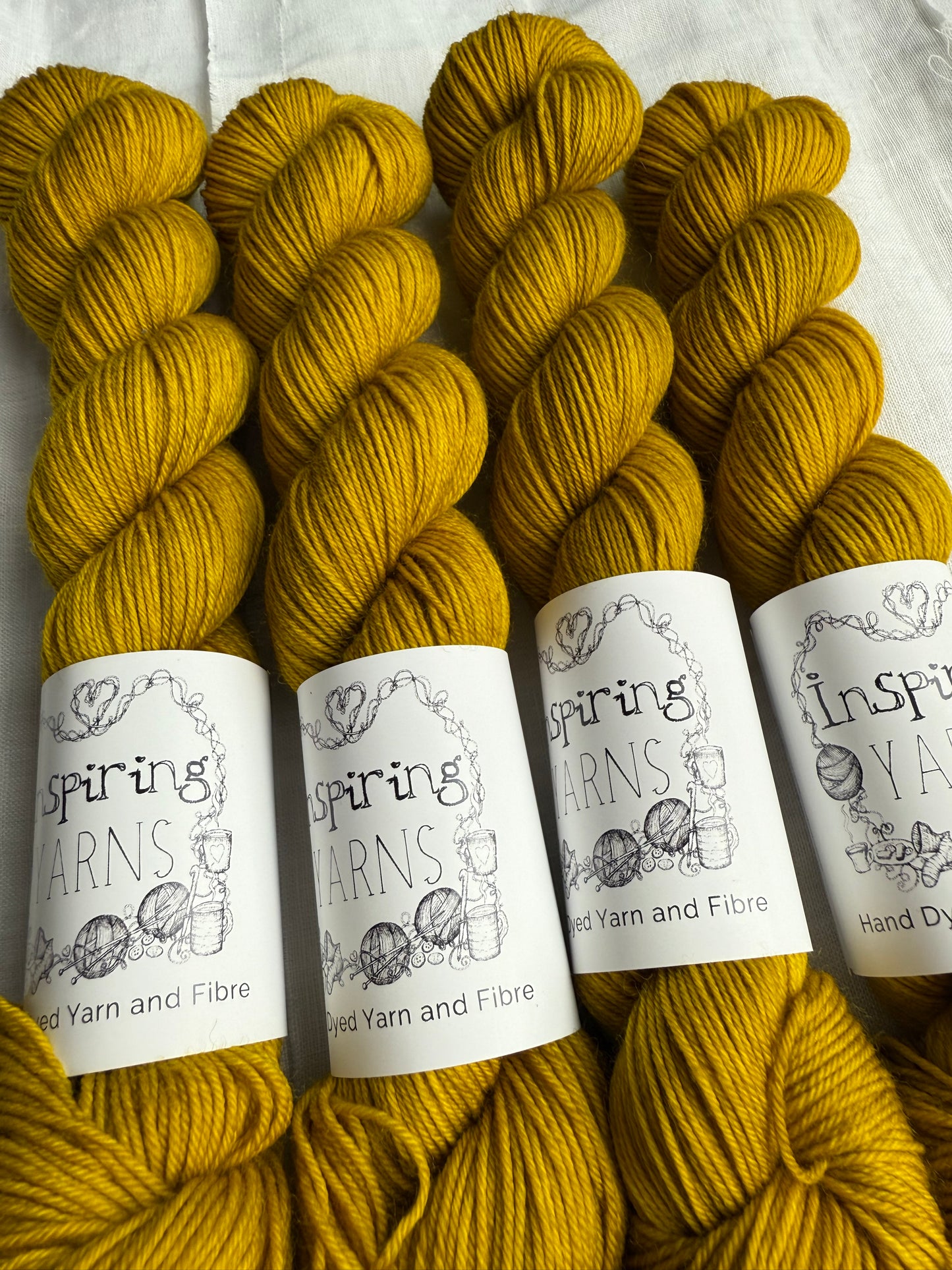 up close of four skeins of yarn in a tonal yellow with black and white inspiring yarns labels.
