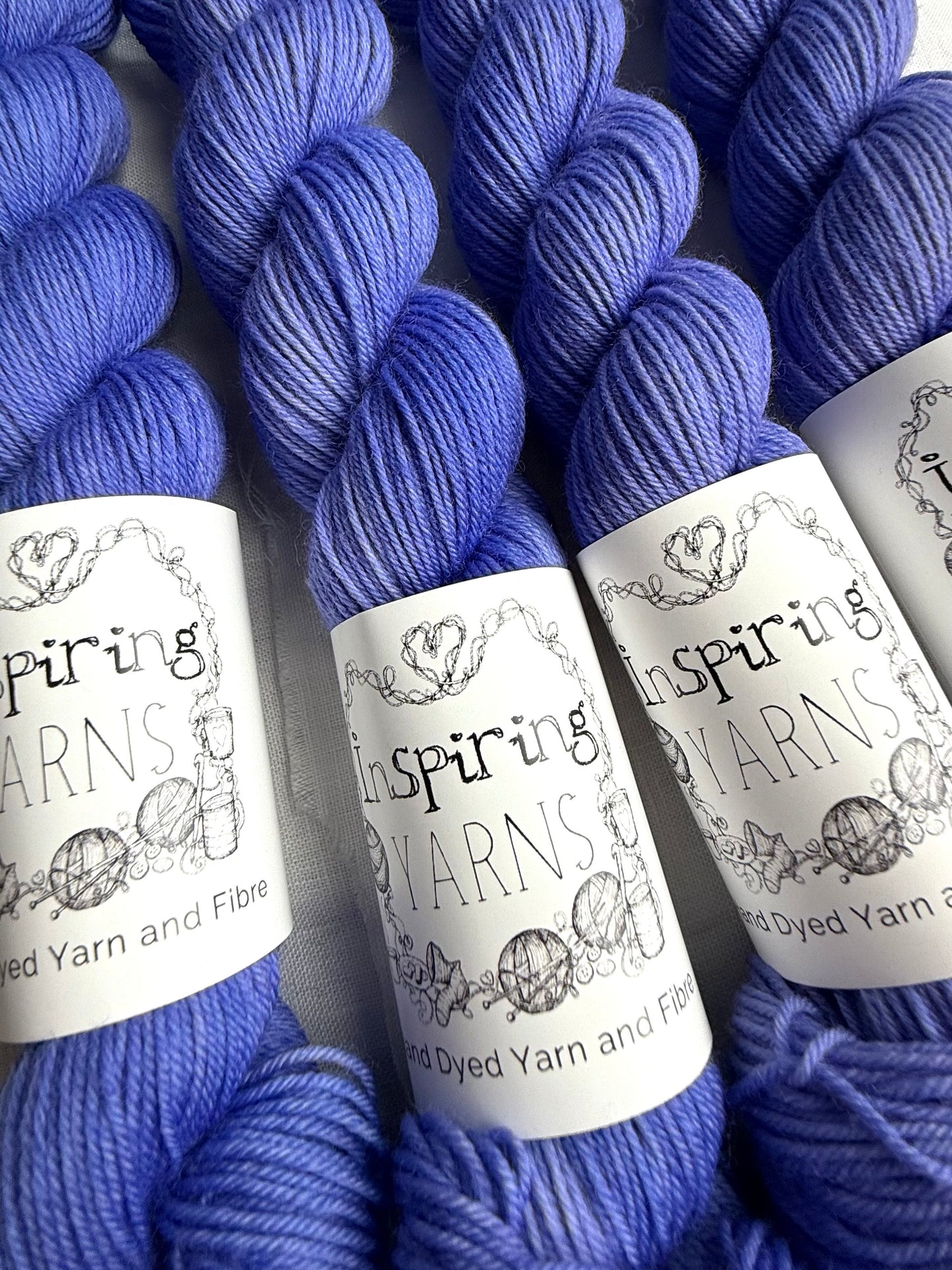 up close of four skeins of bright blue yarn with black and white inspiring yarns labels around them on a plain white fabric background.