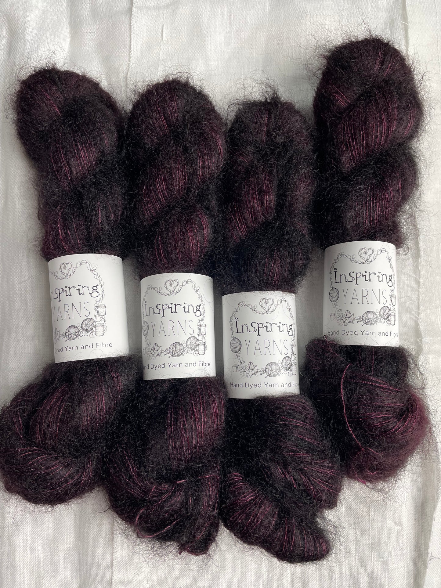Four skeins of dark burgundy coloured Kid Mohair Silk Lace labelled Inspiring Yarns on a white linen background.